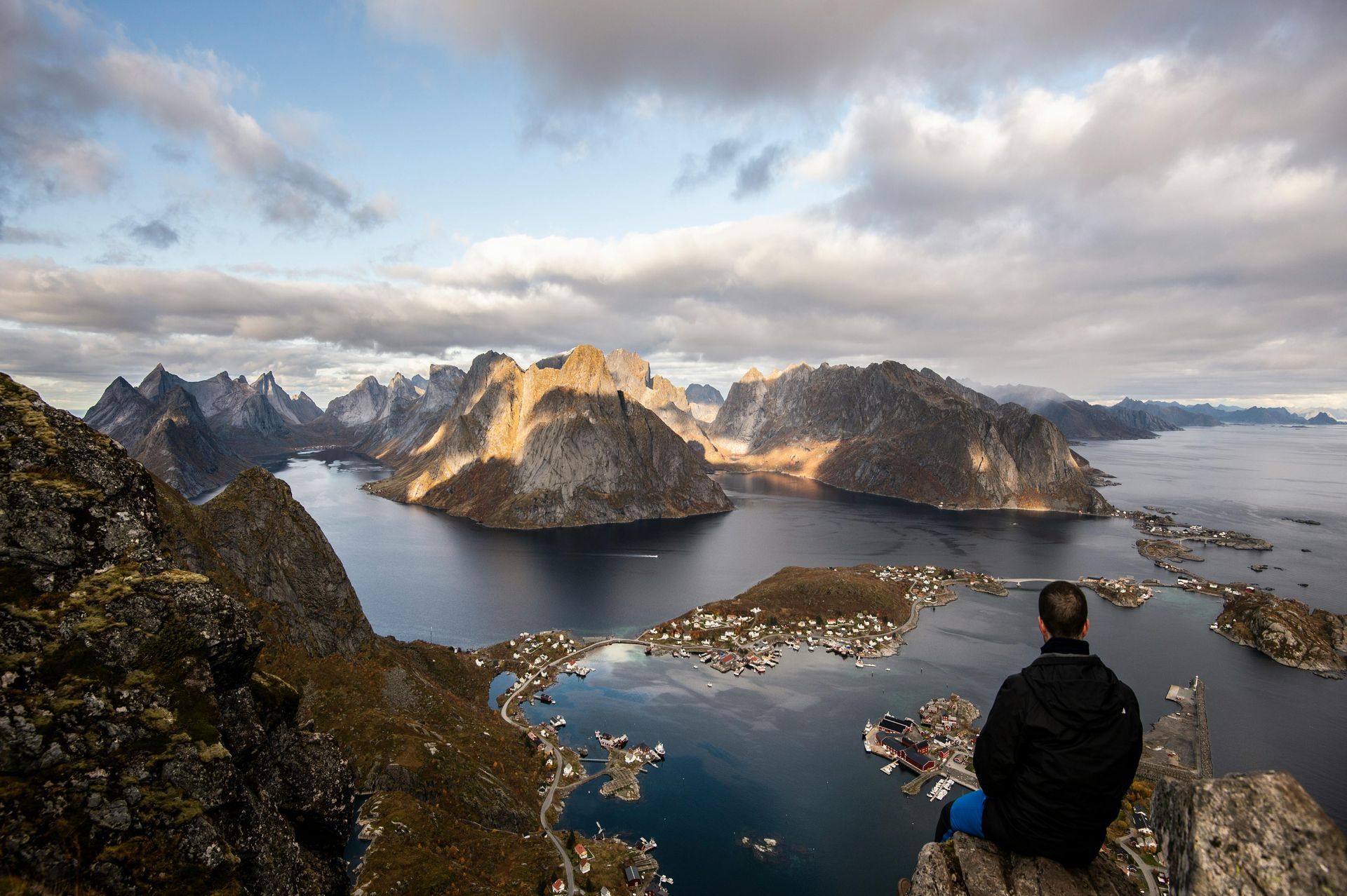 A man is sitting on top of a mountain overlooking a lake in Norway.