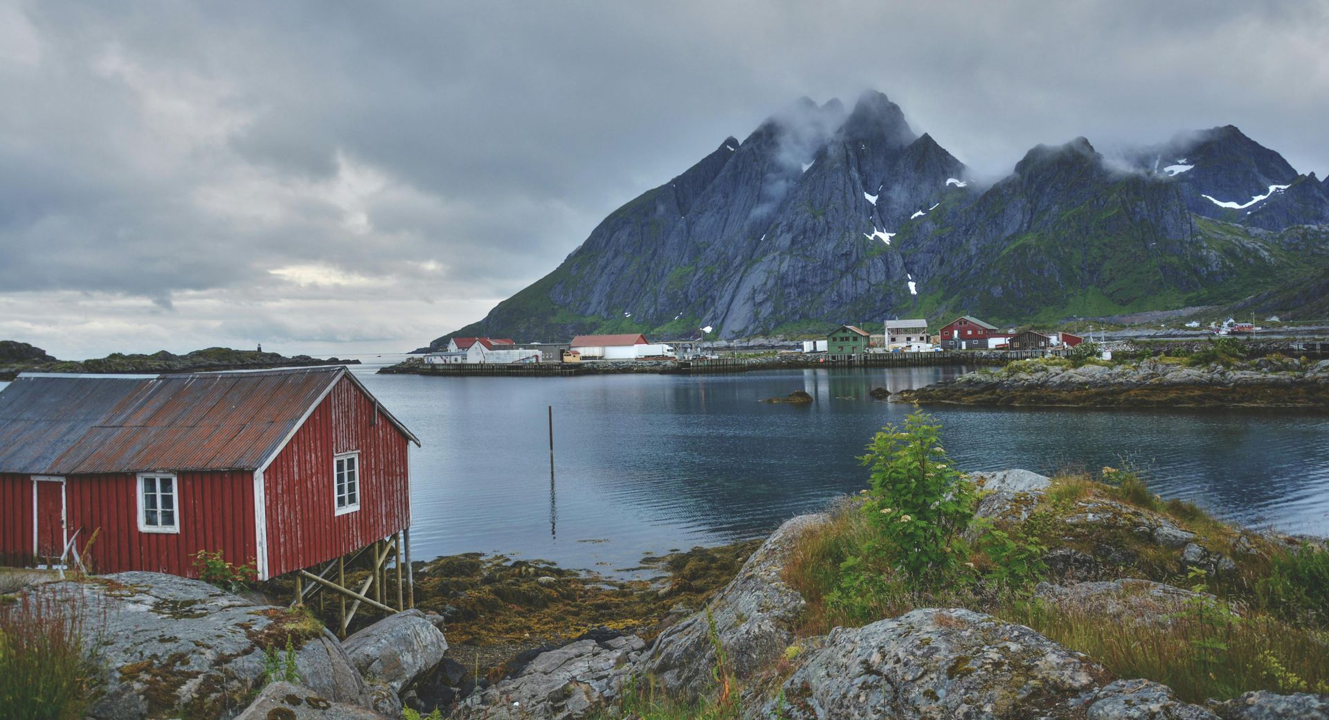 A red house is sitting on the shore of a lake with mountains in the background in Norway.