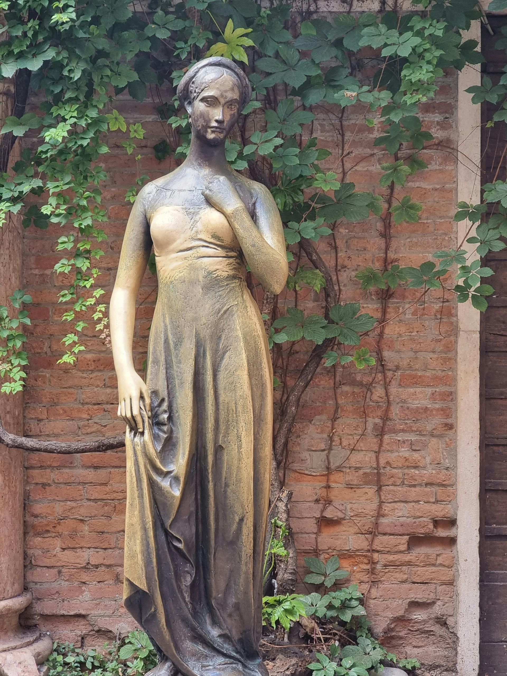 A statue of a woman in a gold dress is standing in front of a brick wall in Verona, Italy.