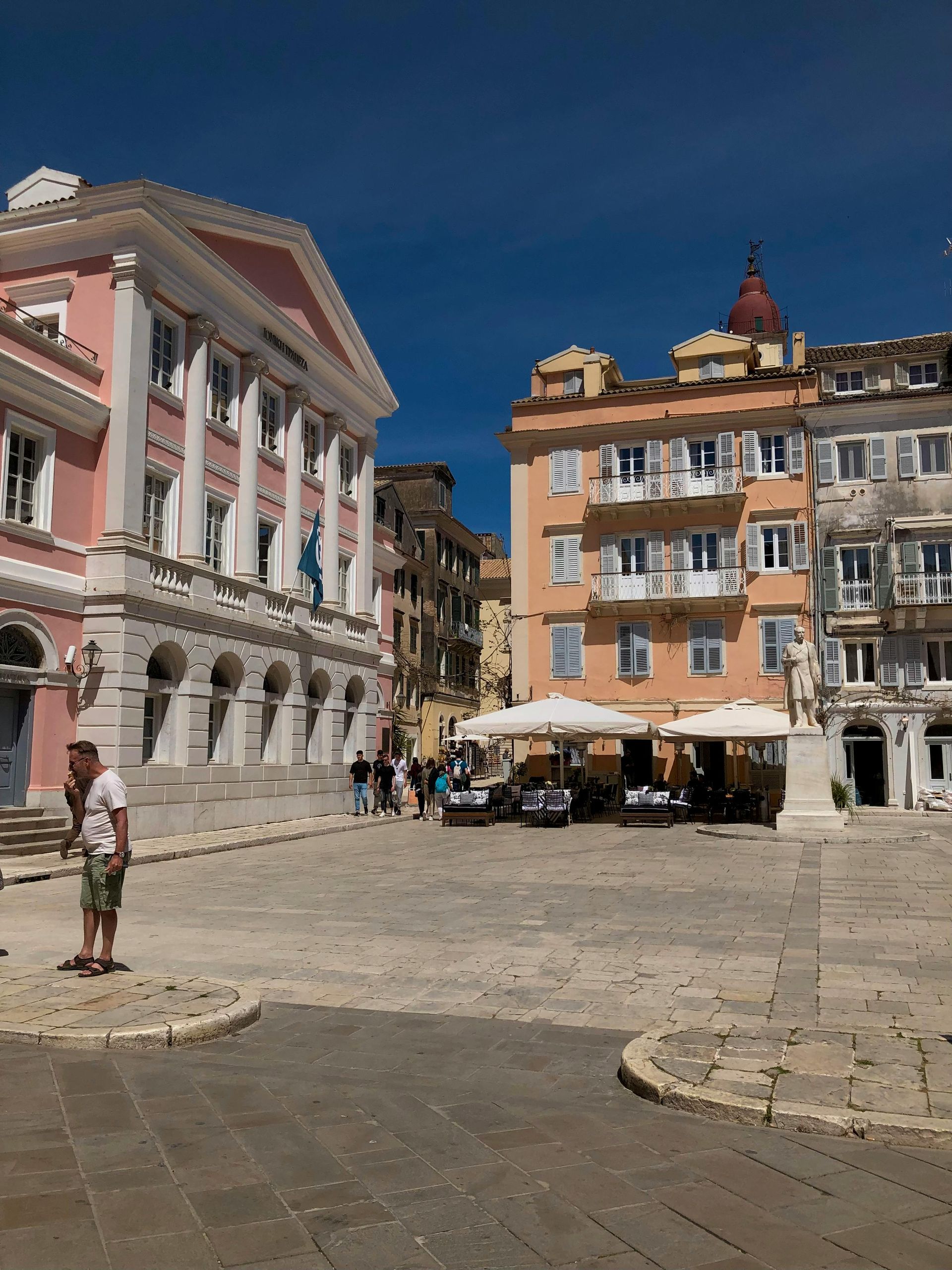 A man is standing in front of a large building in Corfu, Greece.