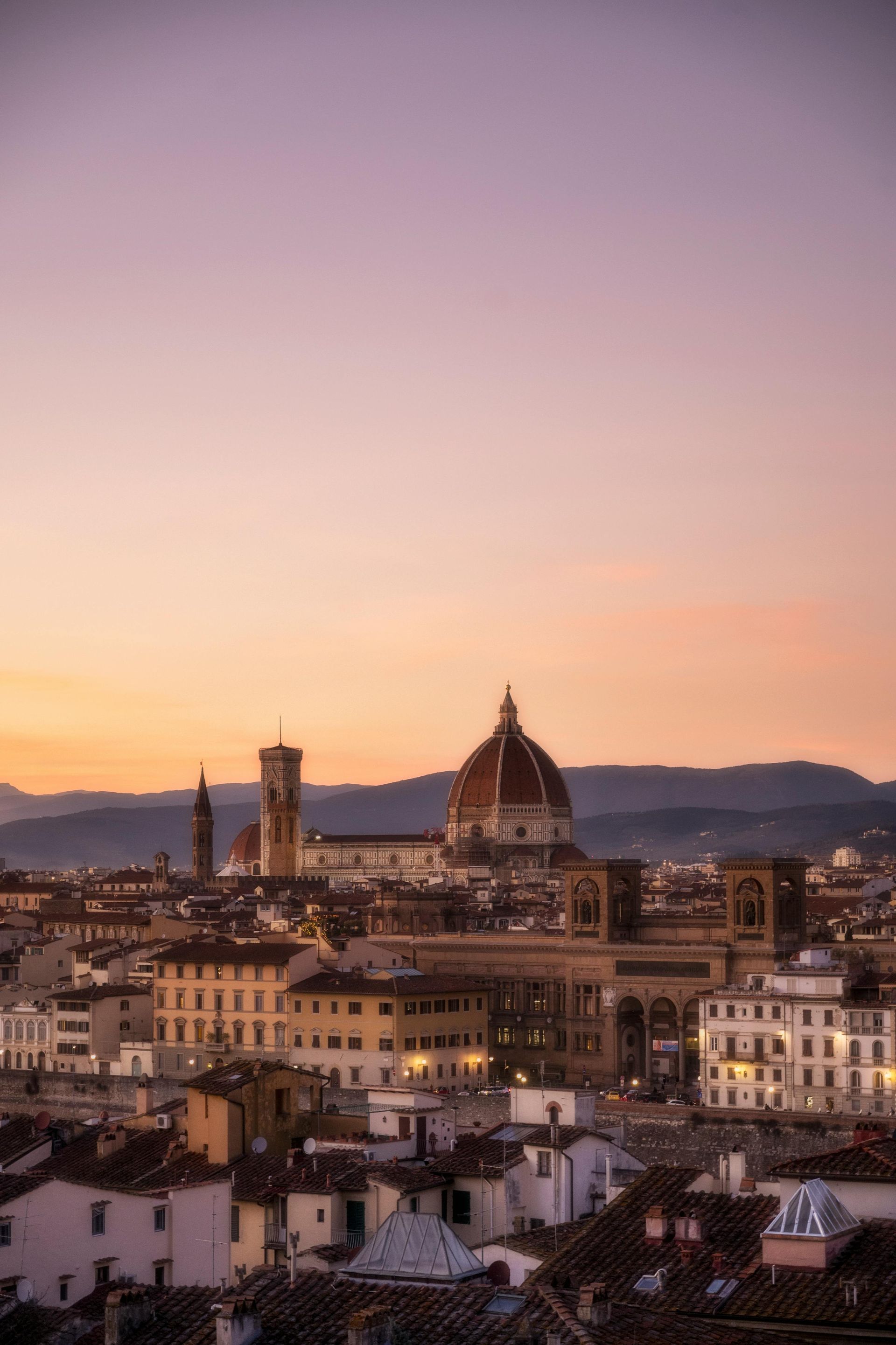 An aerial view of a city at sunset with a dome in the background in Florence, Italy.