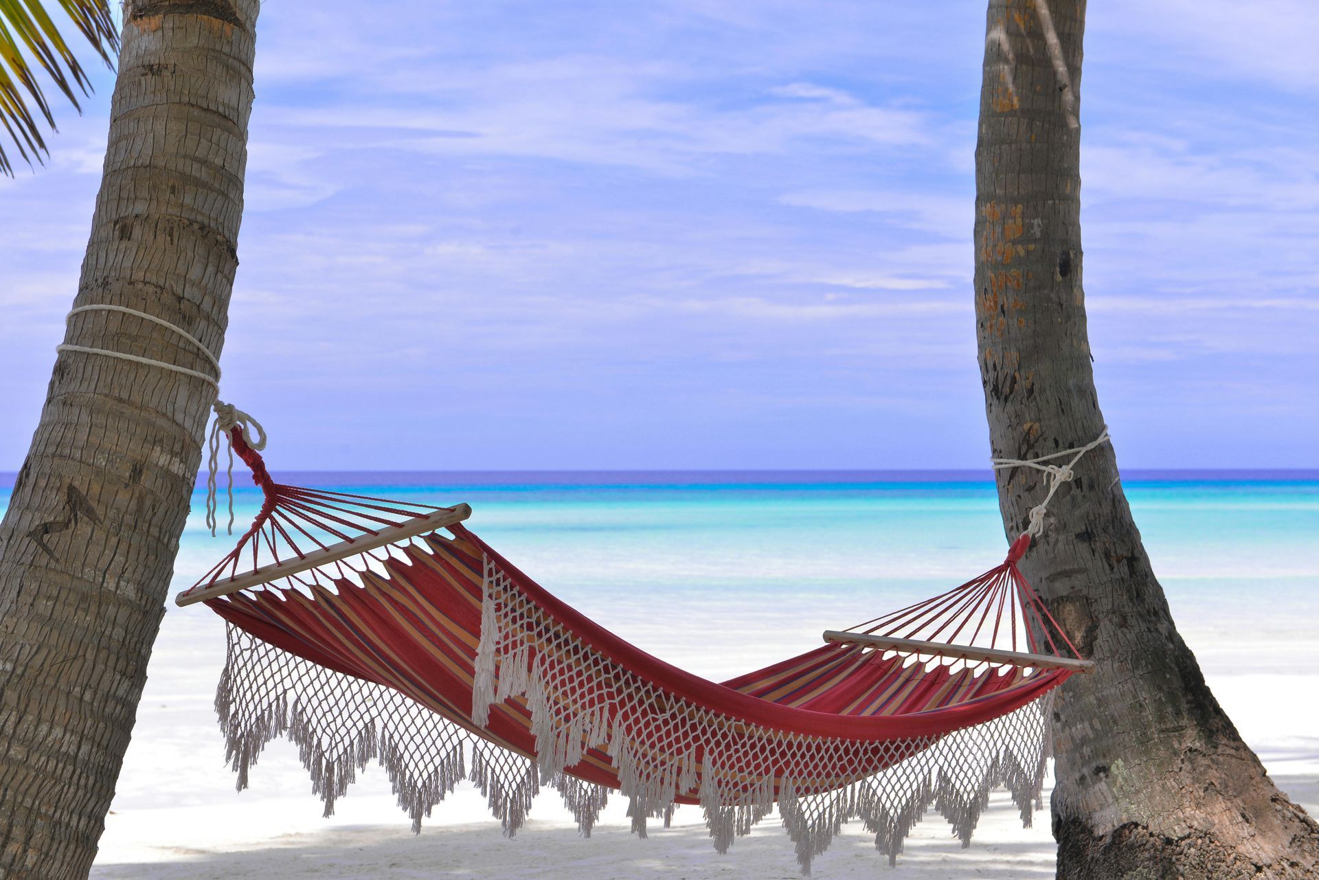 A hammock is hanging between two palm trees on a beach in the Caribbean.