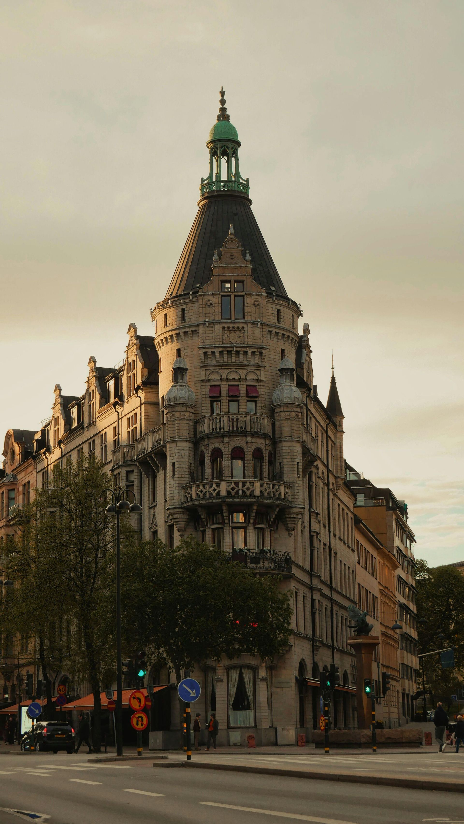 A large building with a clock tower on top of it is on the corner of a city street in Sweden.