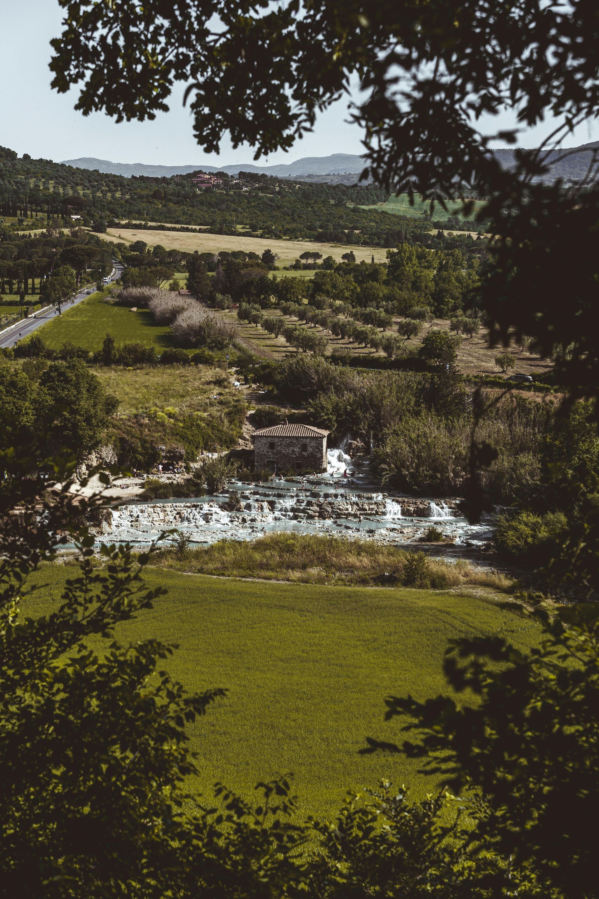 A river flowing through a lush green field surrounded by trees in Tuscany, Italy.