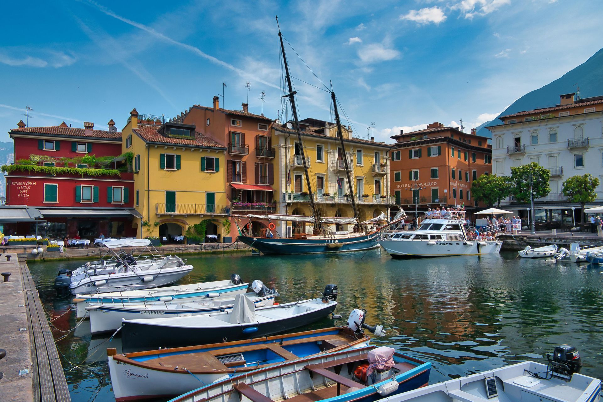 Boats are docked in the harbor of Lake Garda with buildings in the background in Italy.