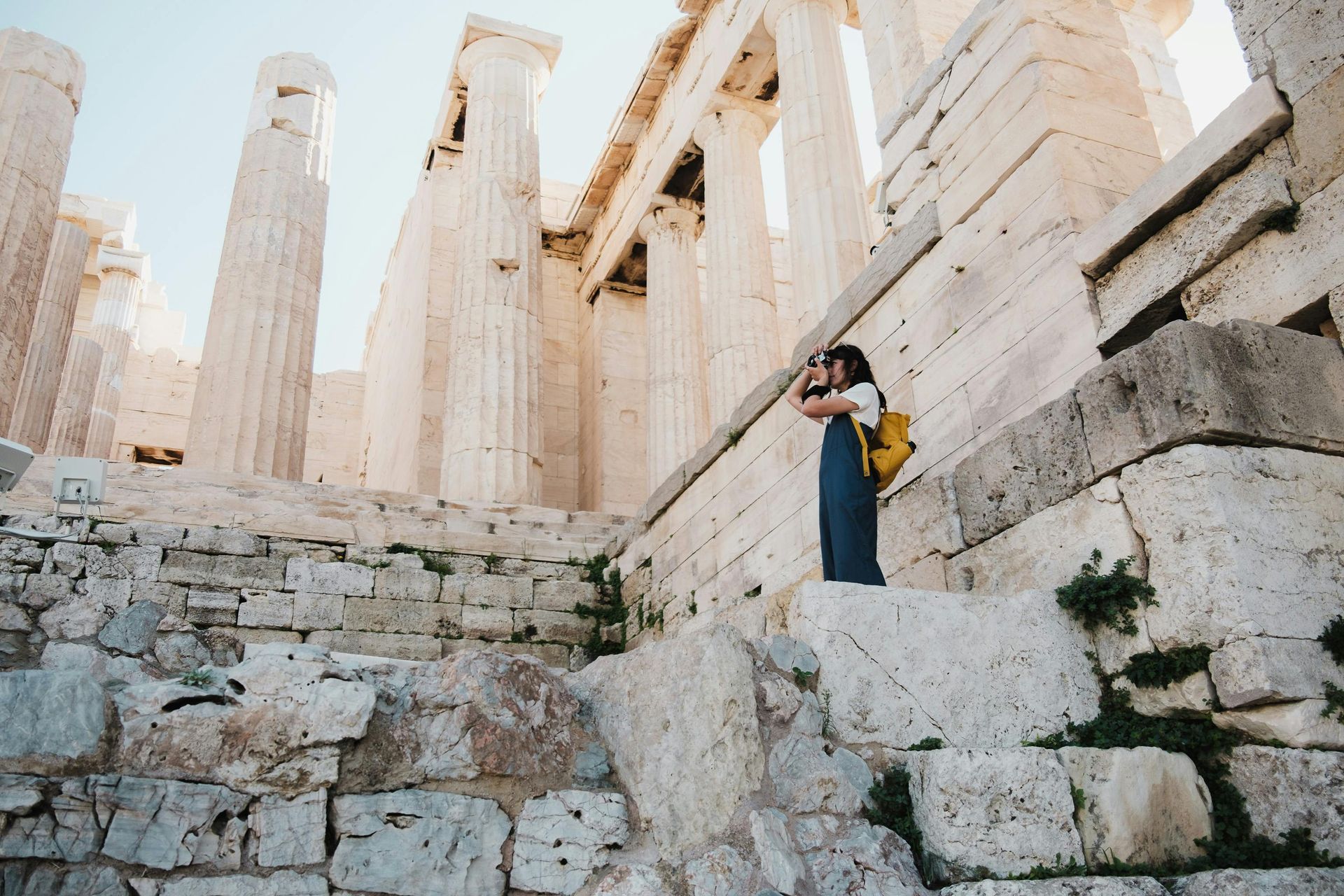 A woman is standing on the steps of an ancient building in Athens, Greece.