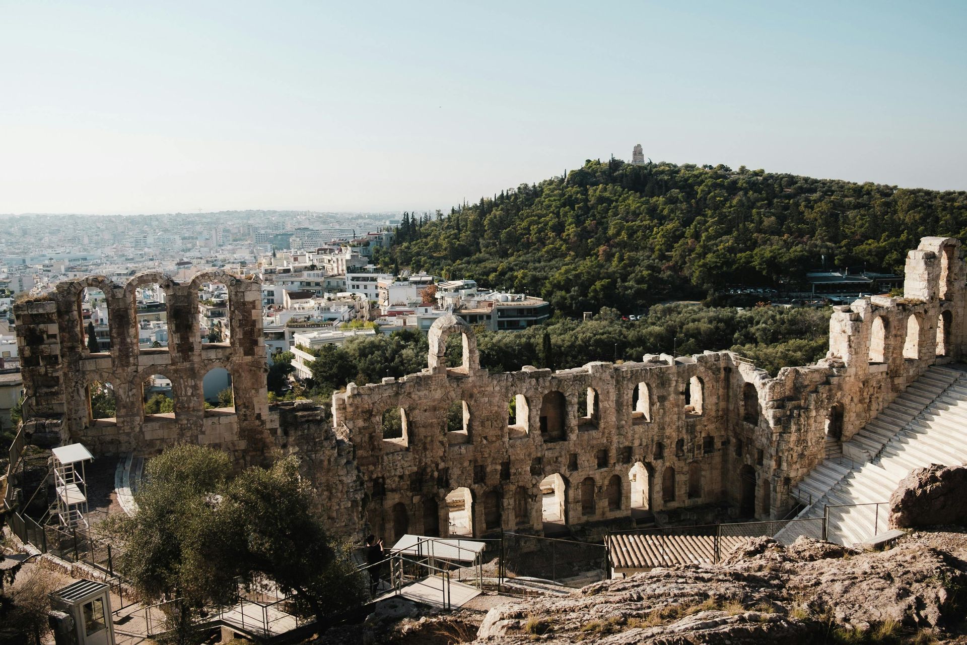 An aerial view of an ancient amphitheater surrounded by trees and Athens, Greece.