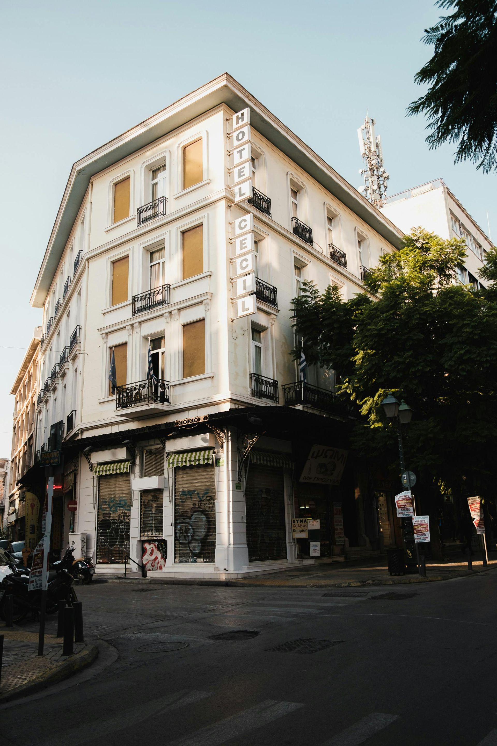 A large white building is on the corner of a city street in Athens, Greece.