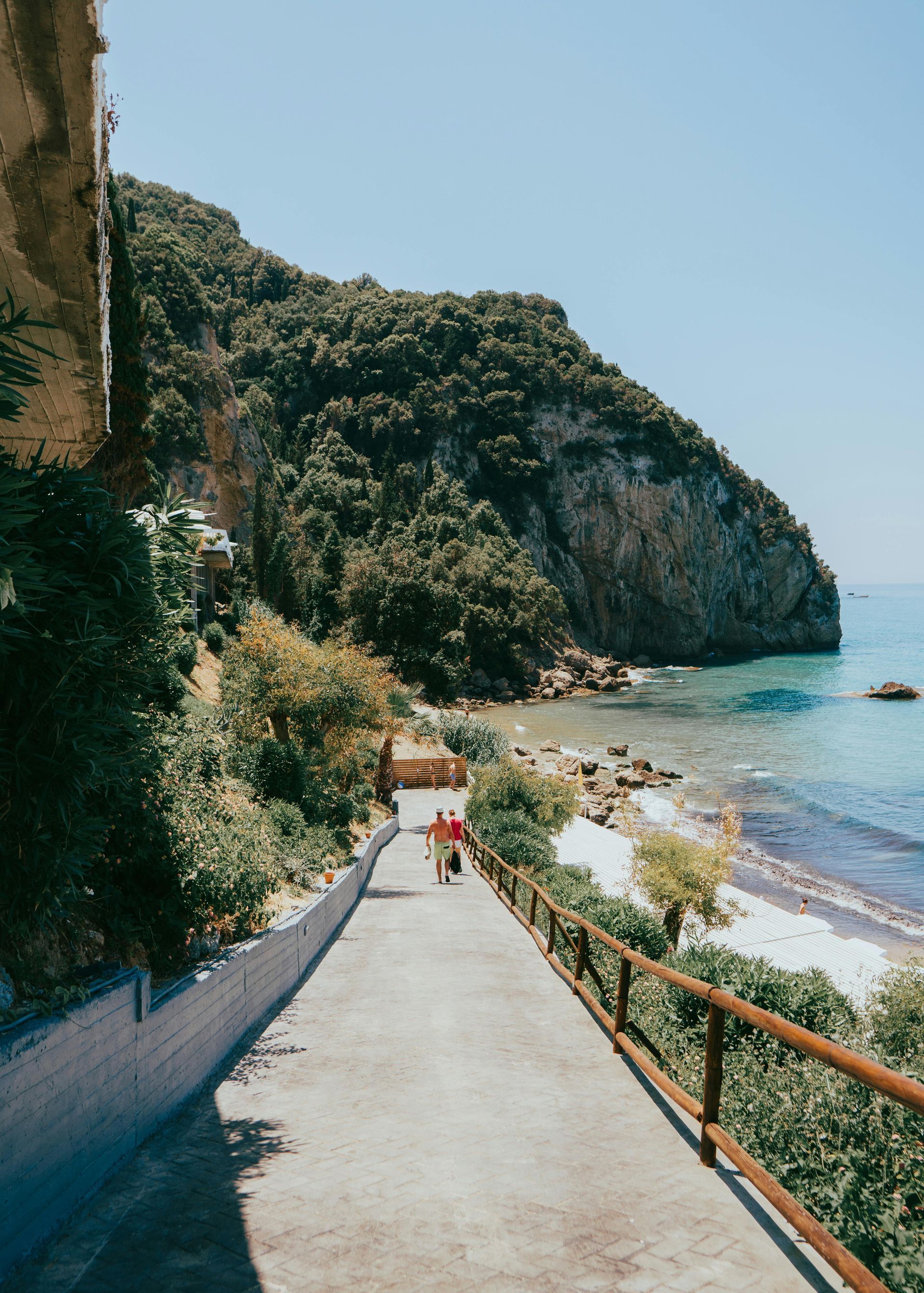 A person is walking down a path towards the ocean in Corfu, Greece.