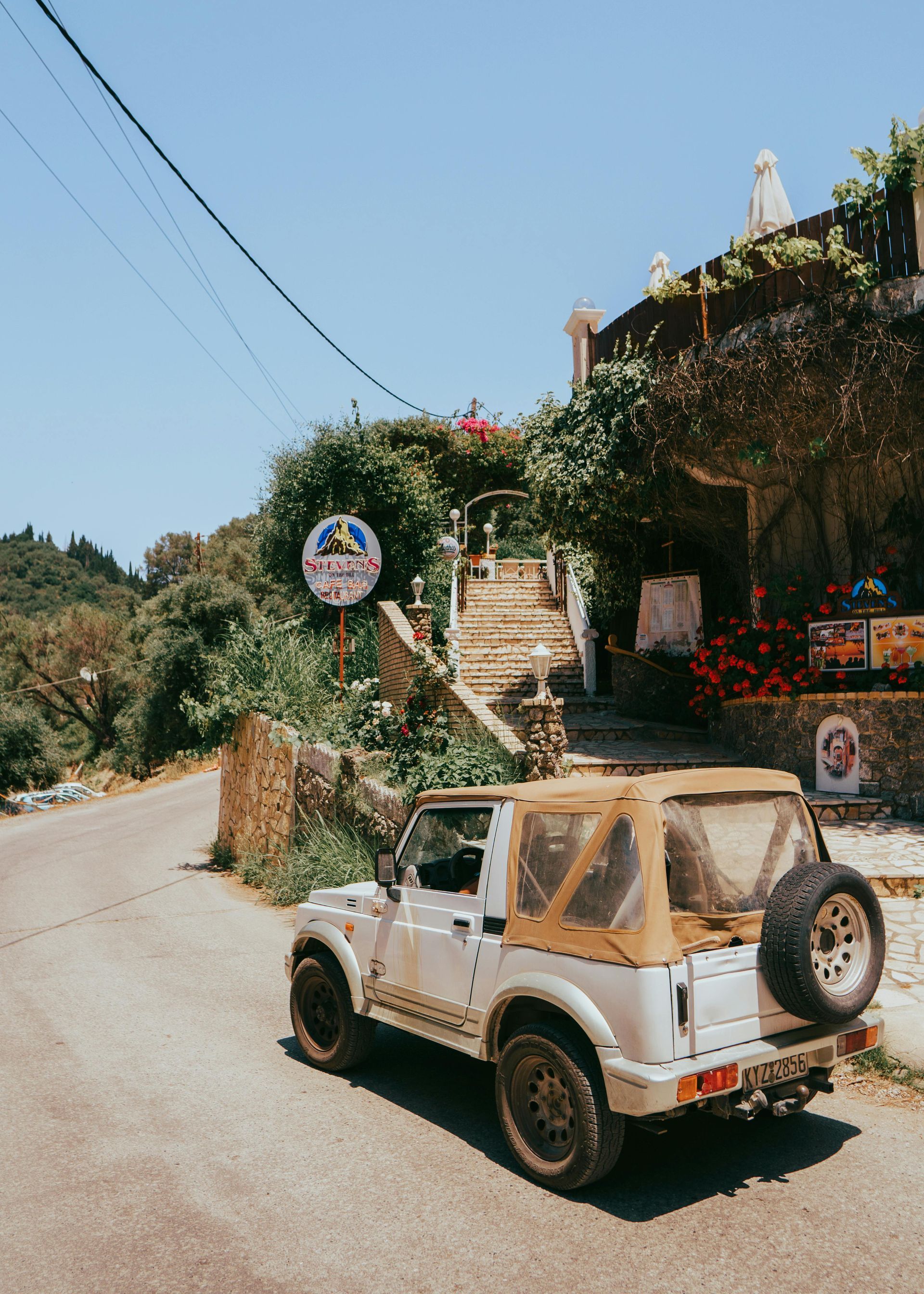 A white jeep is parked on the side of the road in front of a building in Corfu, Greece.