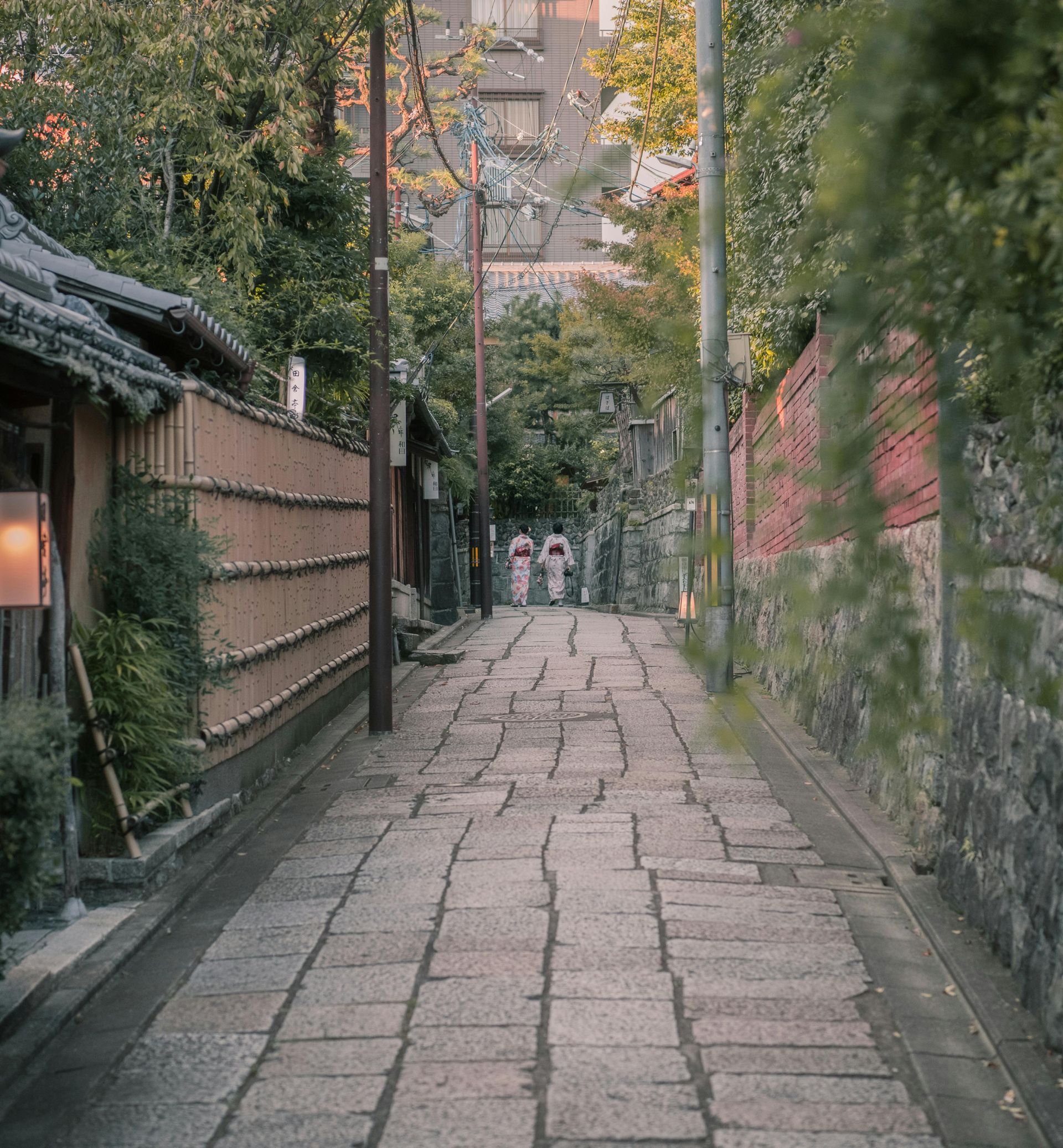 A couple of people are walking down a narrow brick street in Japan.