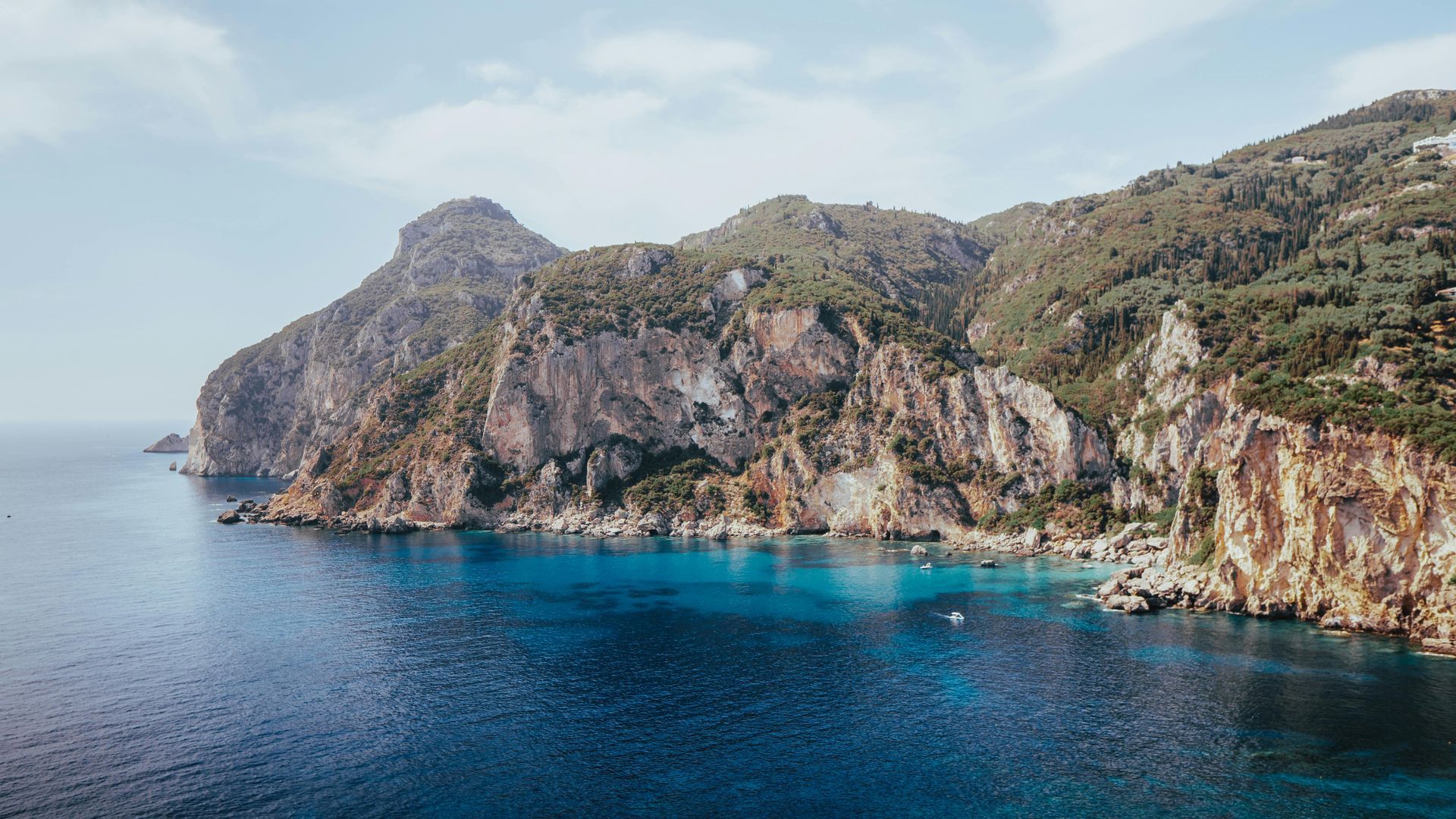 An aerial view of a cliff overlooking a body of water with mountains in the background in Corfu, Greece.