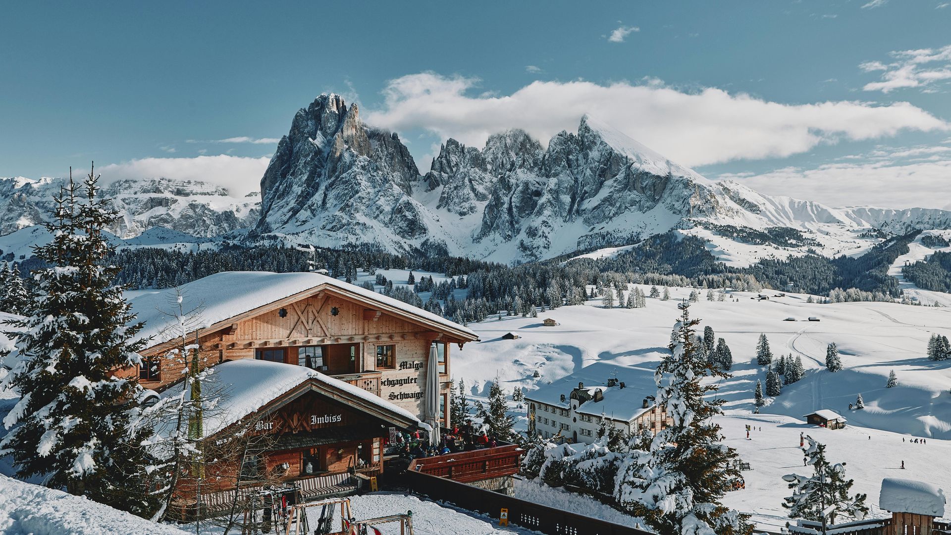 A snowy landscape with a house in the foreground and The Dolomites in the background in Italy.