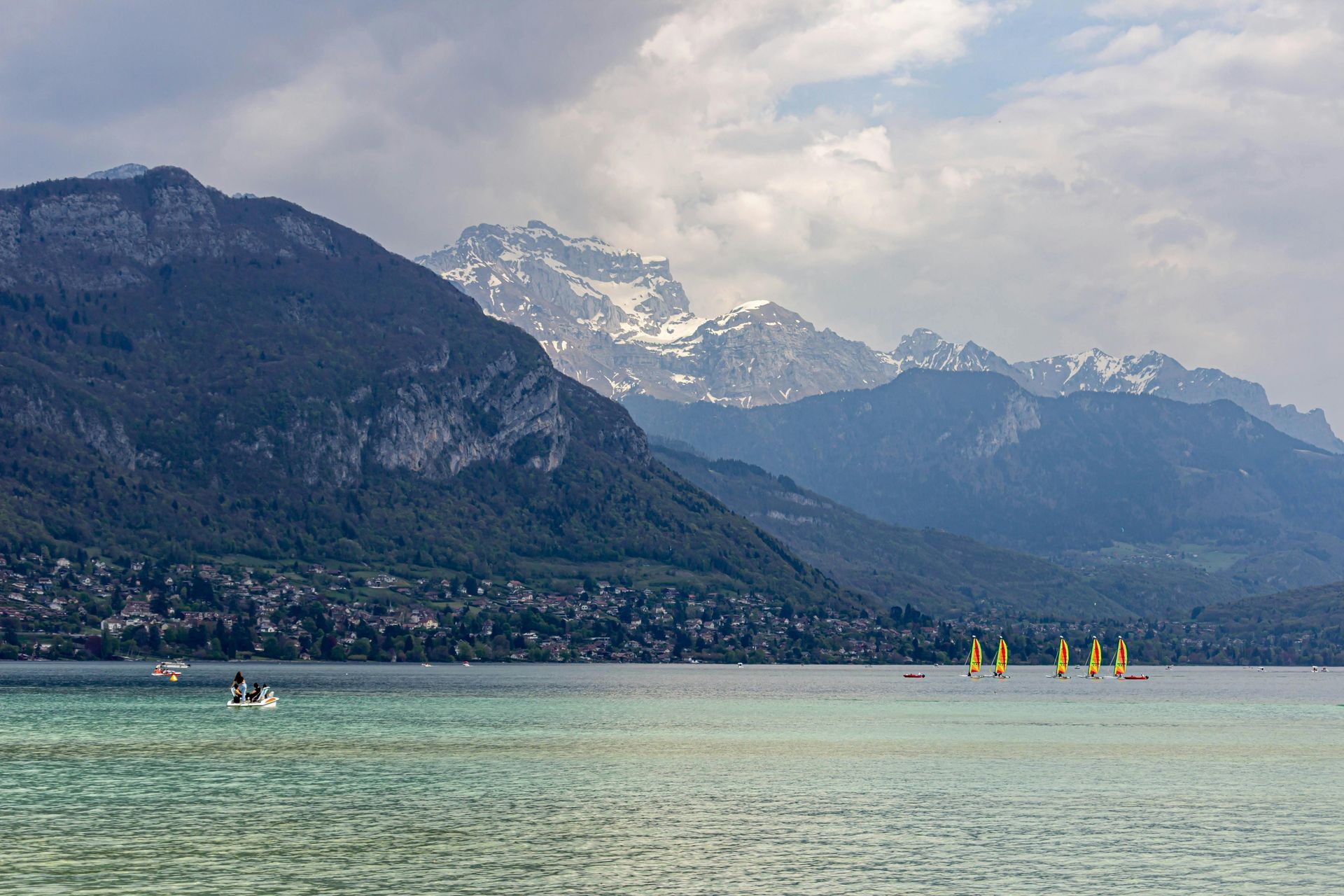 A group of sailboats are floating on lake Annecy with mountains in the background in Annecy, France.