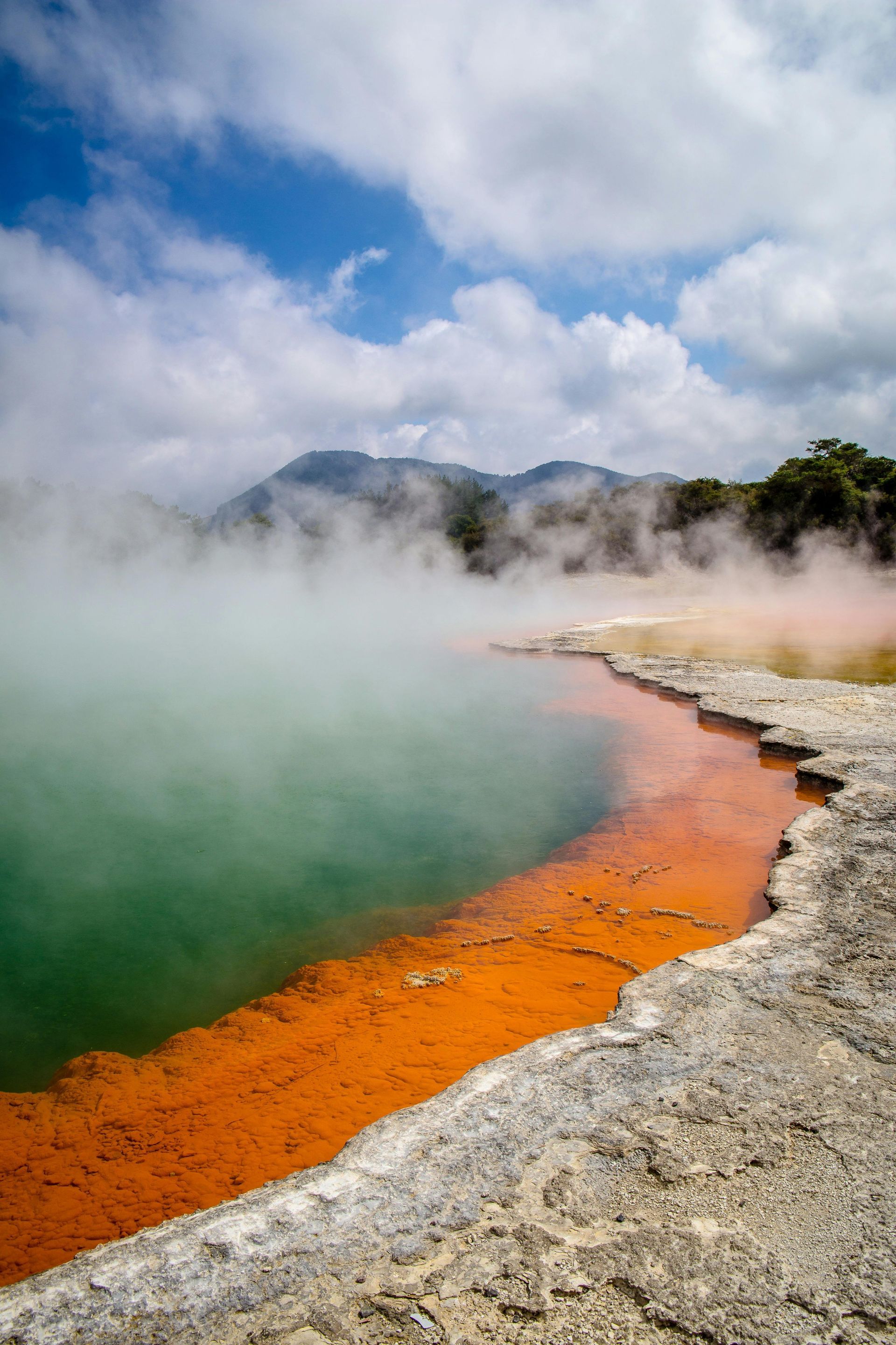 A large body of water with steam coming out of it and mountains in the background in New Zeland.