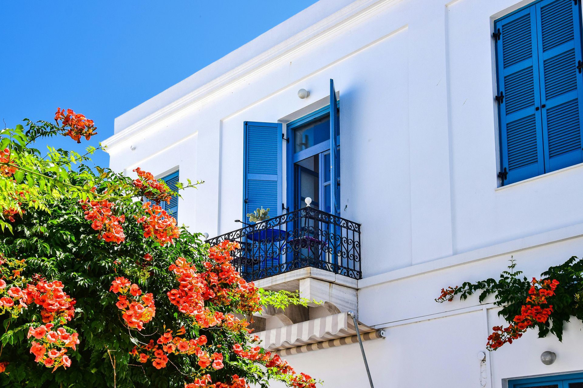 A white building with blue shutters and flowers in front of it in Mykonos, Greece.