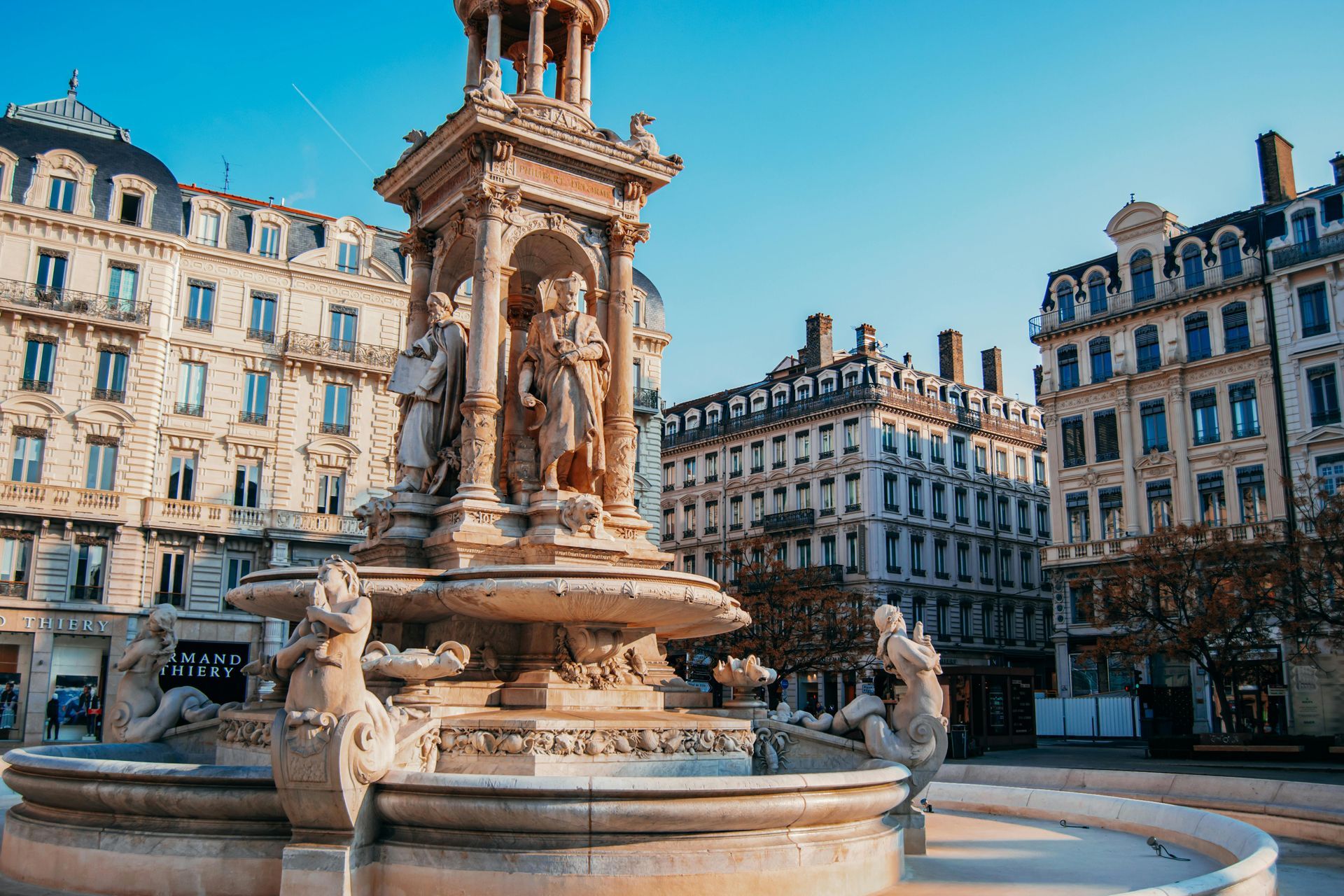 There is a fountain in the middle of Lyon, France with buildings in the background.