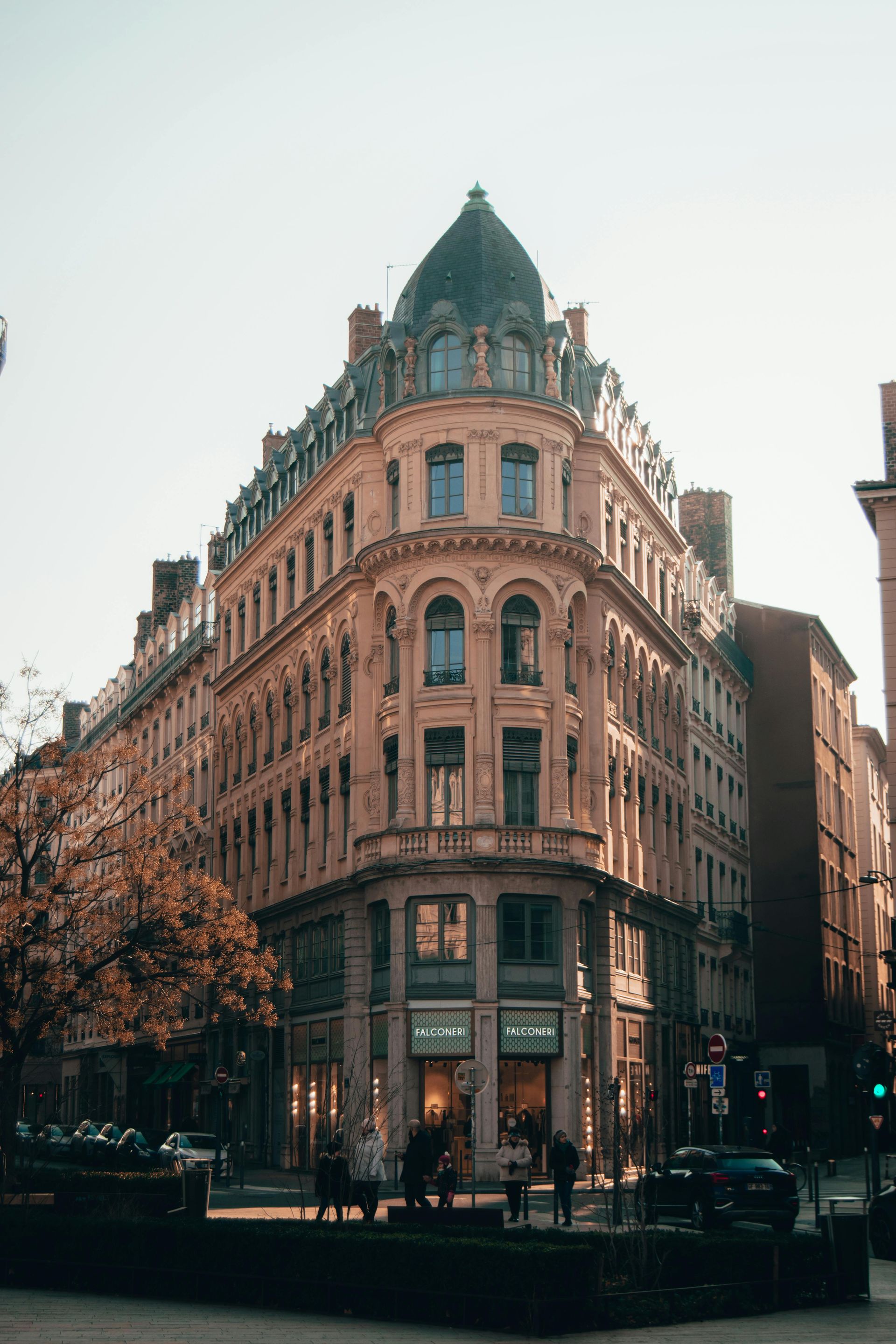 A large building with a dome on top of it is on the corner of a city street in Lyon, France.