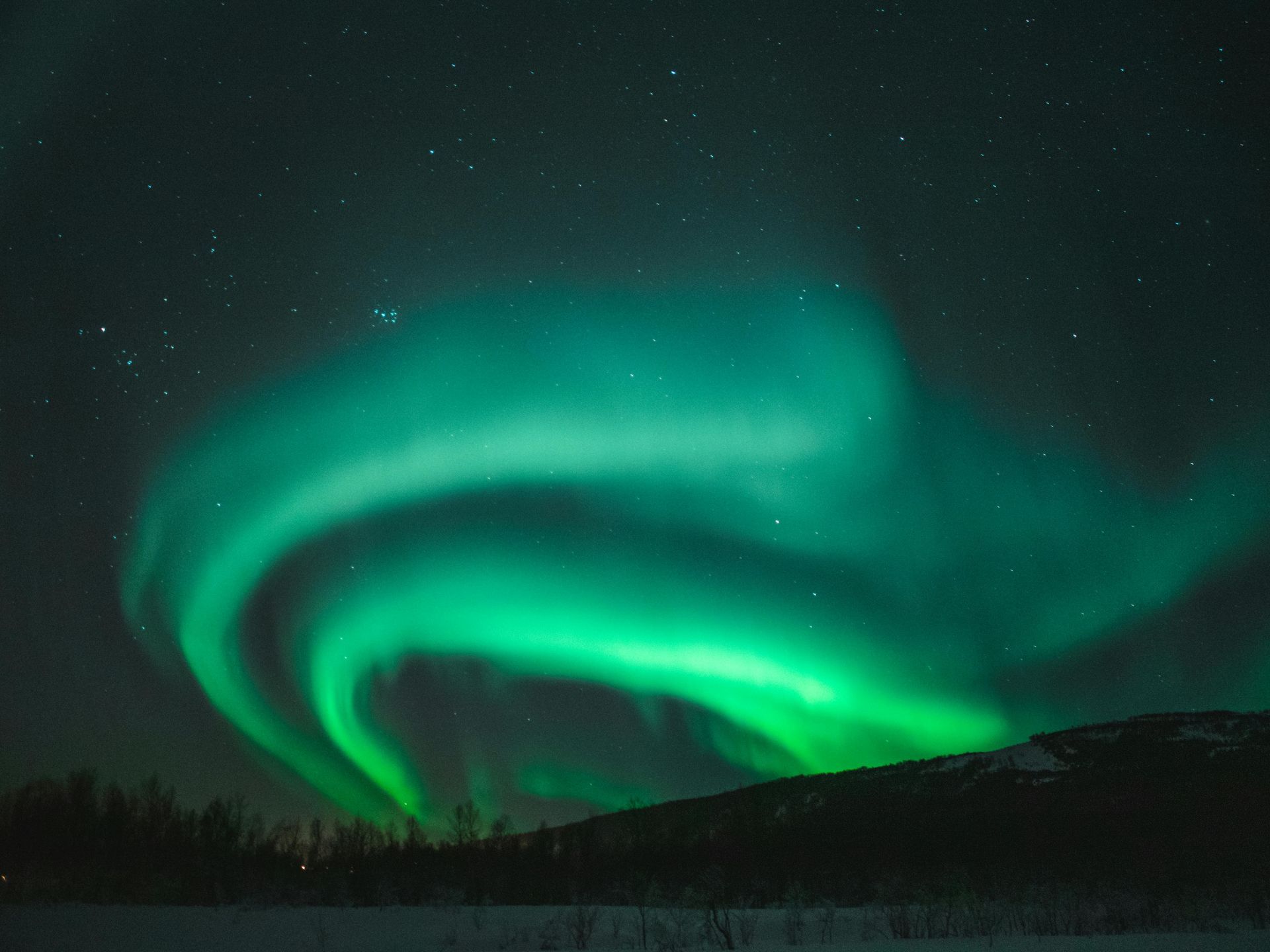 The aurora borealis is dancing in the night sky over a snowy landscape in Norway