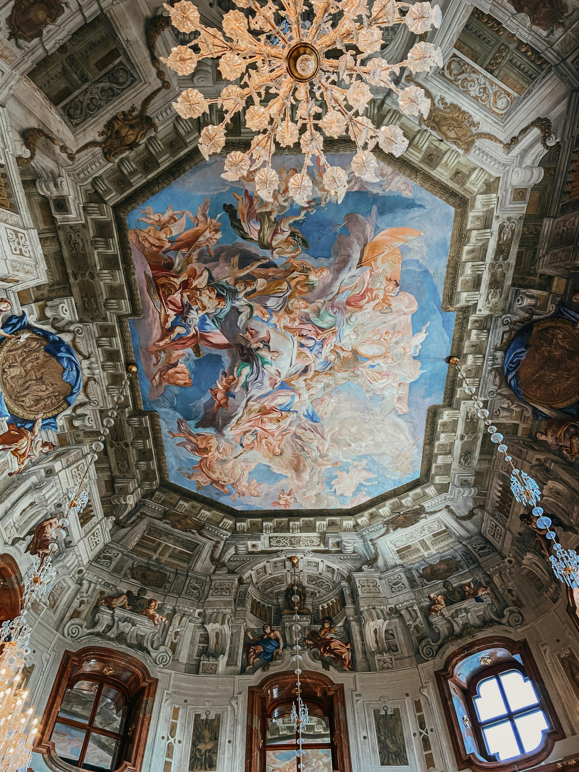 A ceiling with a painting on it and a chandelier hanging from it in Belvedere Palace in Vienna, Austria. 