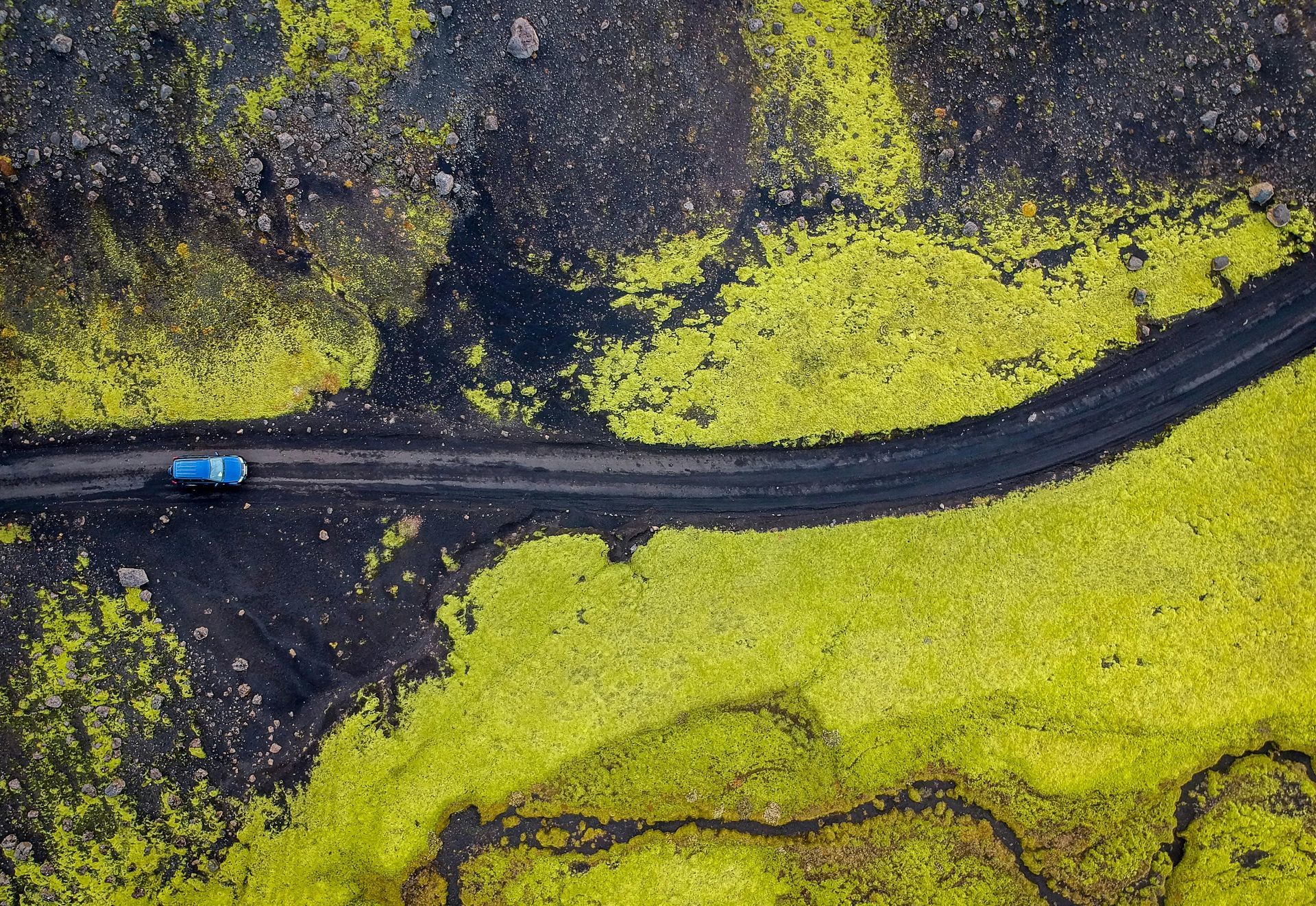 An aerial view of a car driving down a road surrounded by green grass in Iceland.