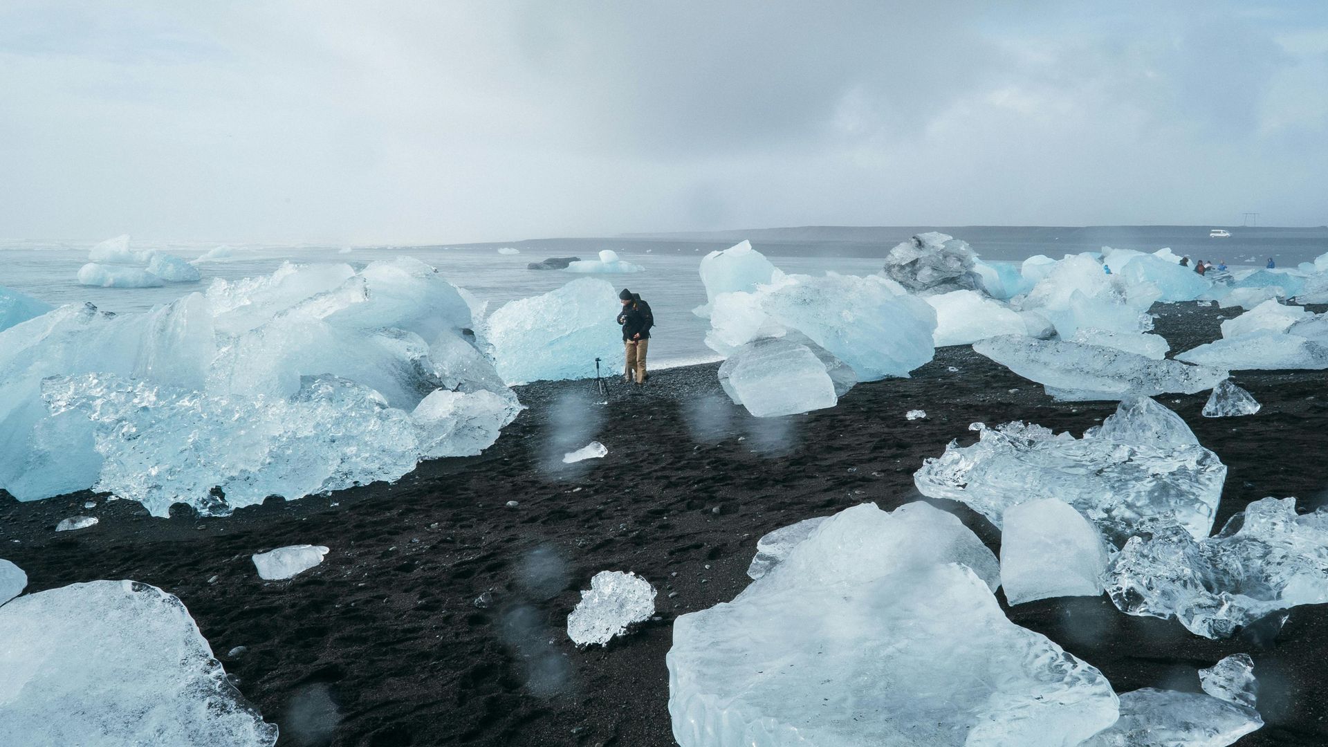 A person is standing on a beach surrounded by ice cubes in Iceland.