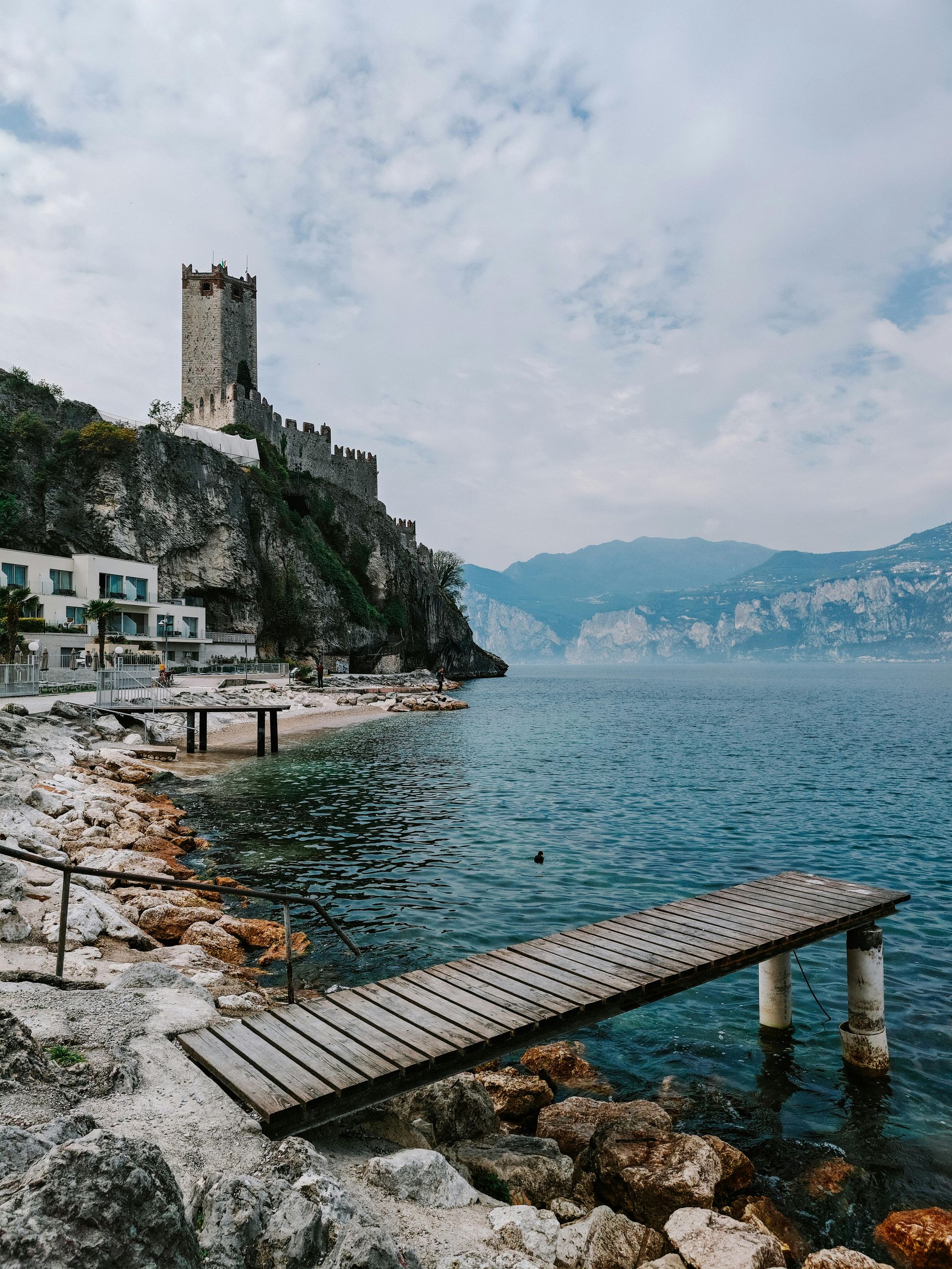 A wooden dock leading to Lake Garda with a castle in the background in Italy.