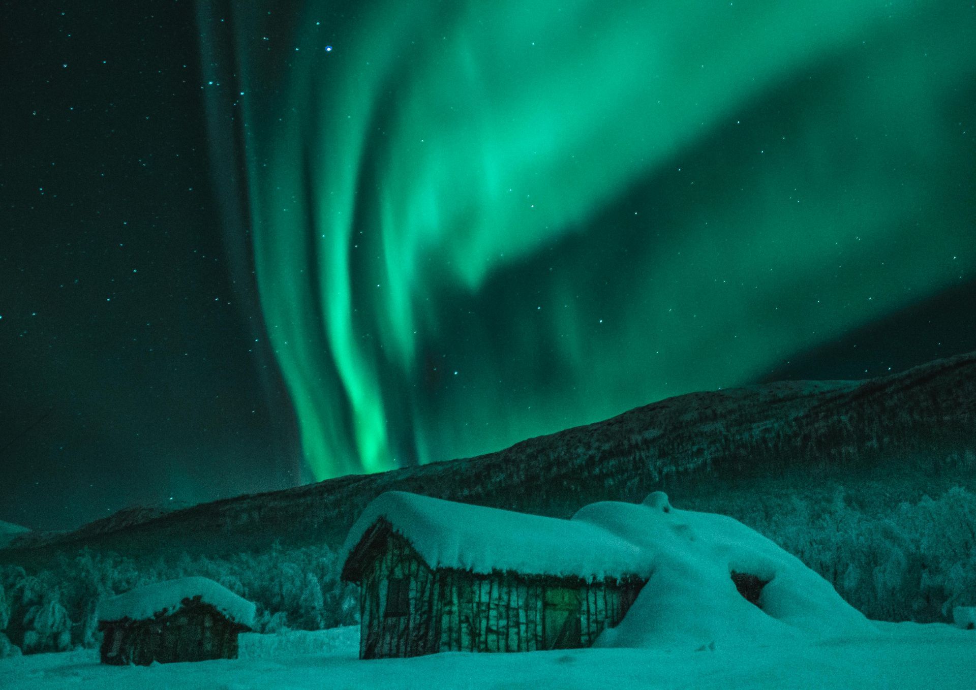 The aurora borealis is shining over a snow covered cabin in Norway.