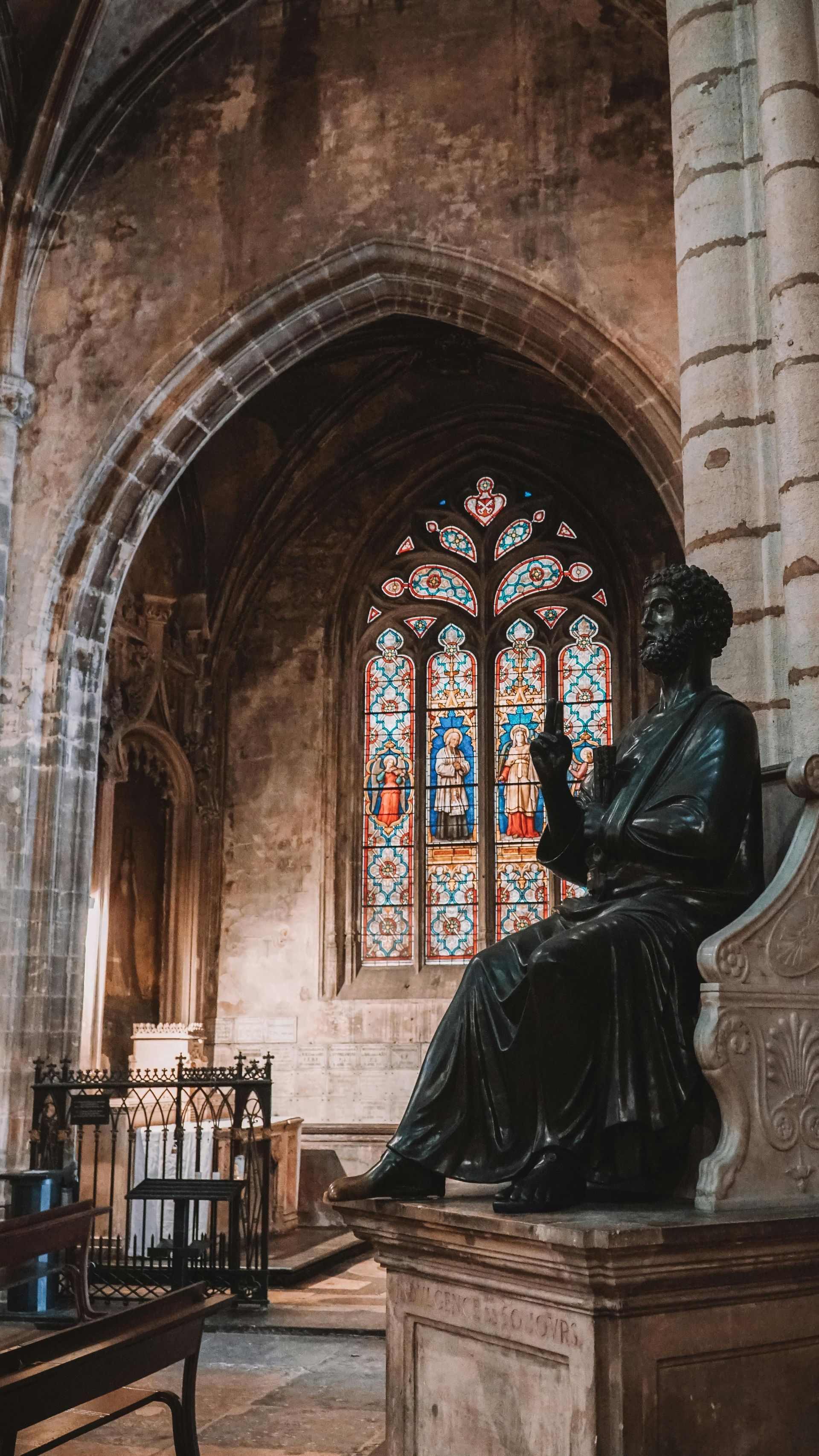 A statue of a man sitting in front of a stained glass window in a church in Lyon, France.