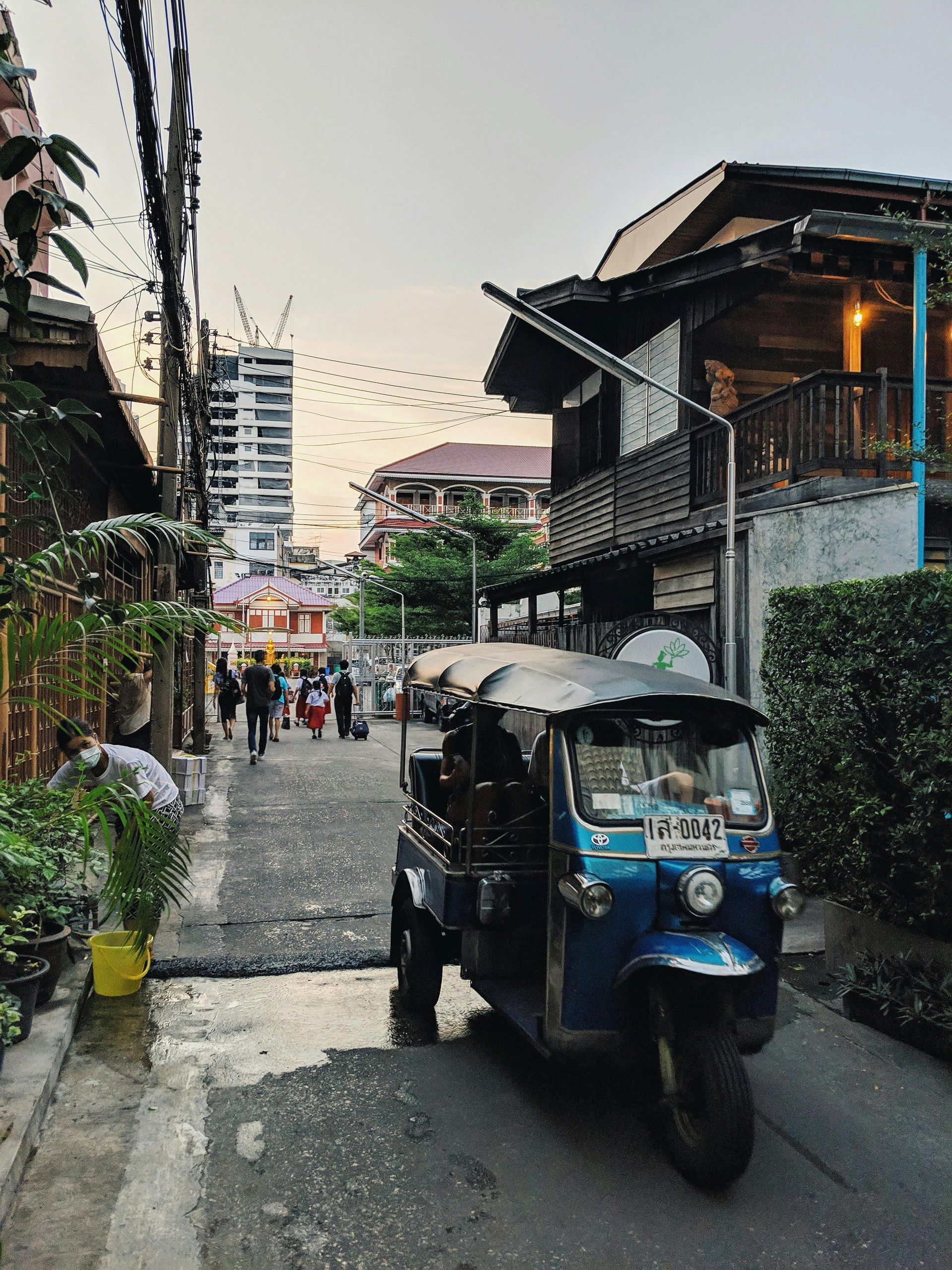 A blue tuk tuk is parked on the side of a street in Thailand.