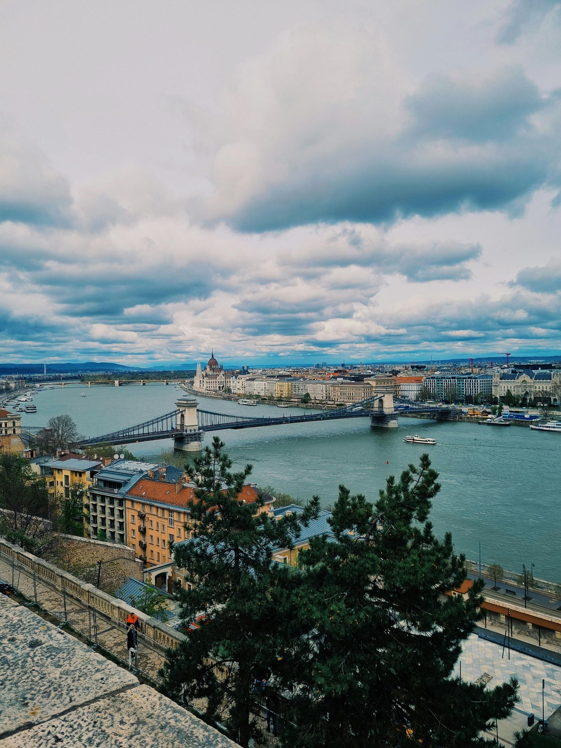 An aerial view of a city with The Danube River in the foreground and a bridge in the background.