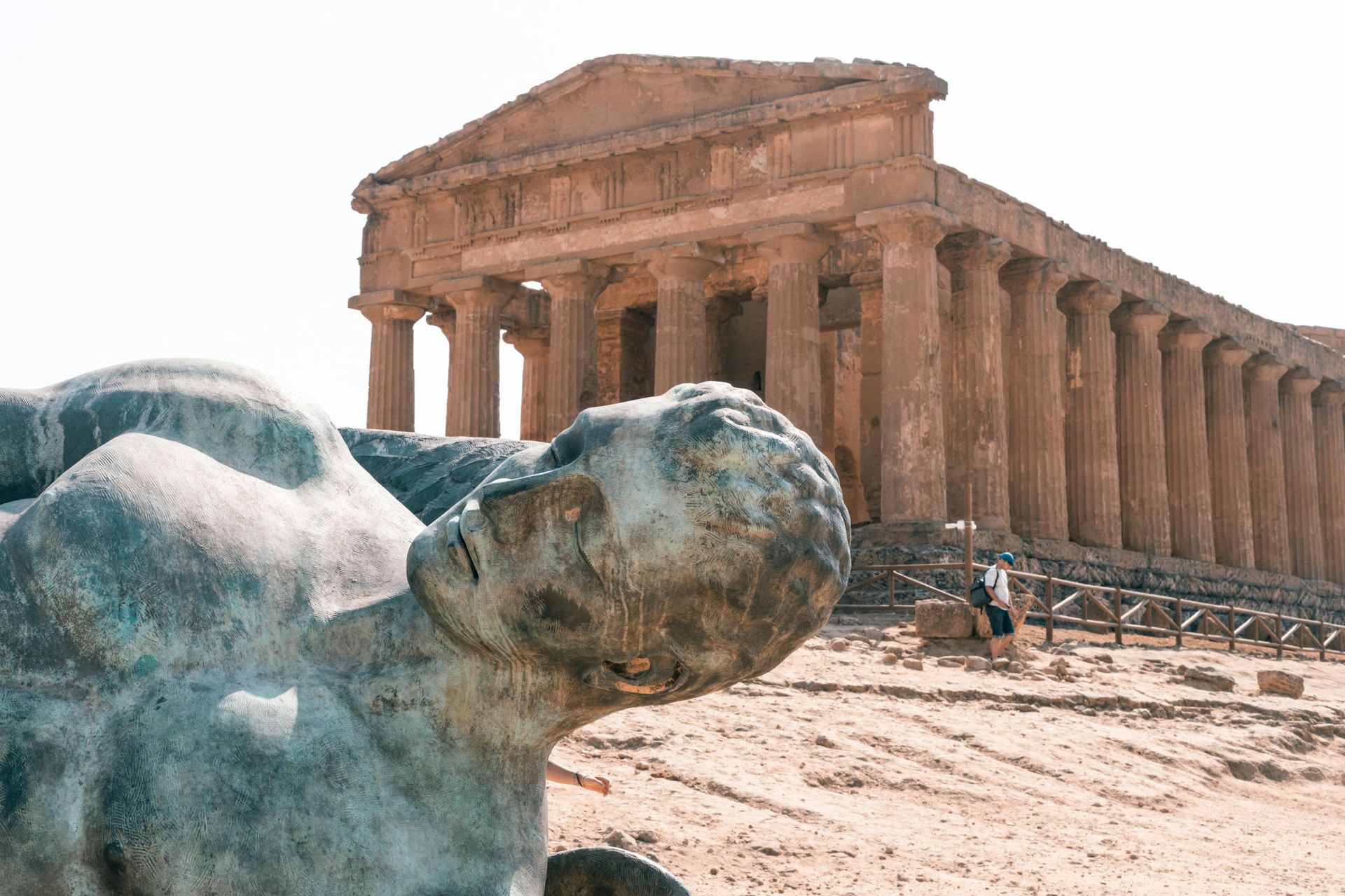 A statue of a man laying down in front of the Temples of Agrigento in Sicily, Italy.