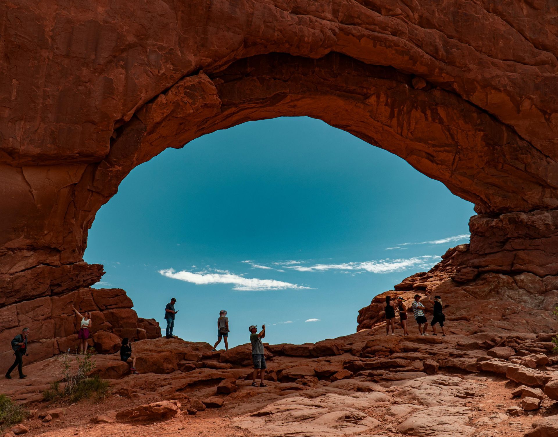 A group of people are standing under an arch in the desert Arches National Park in Utah.