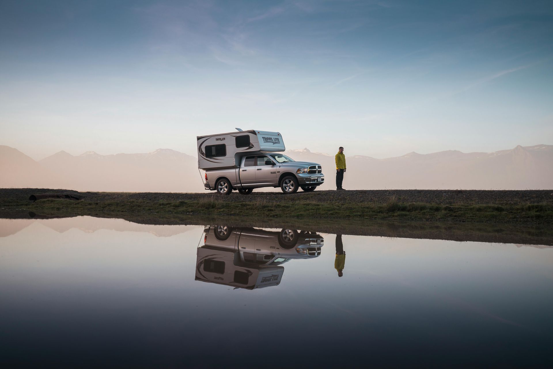 A man is standing next to an rv parked next to a body of water in Iceland.