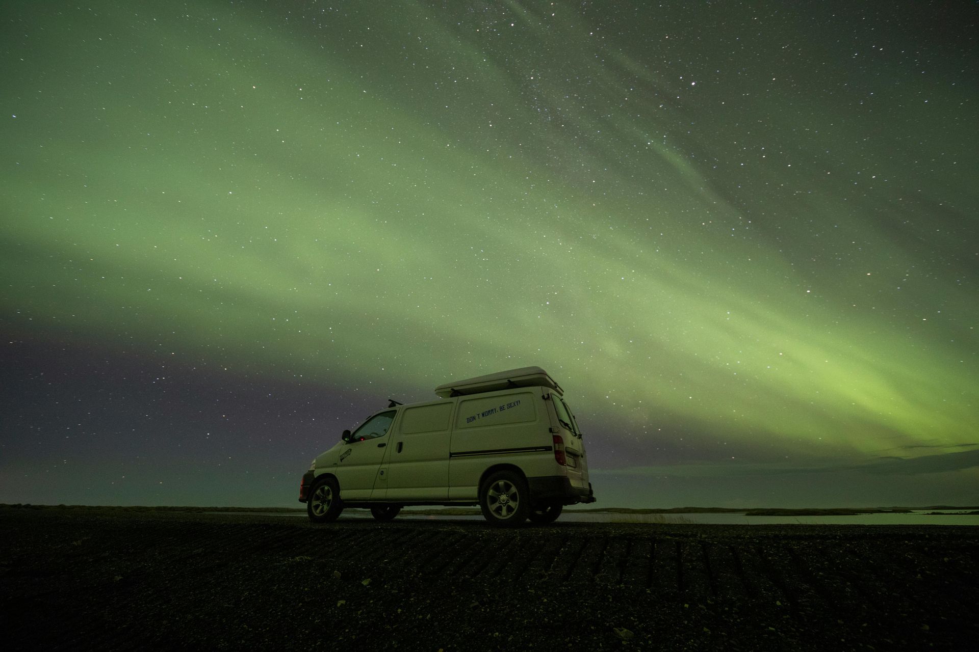 A white van is parked in front of the aurora borealis in Iceland.