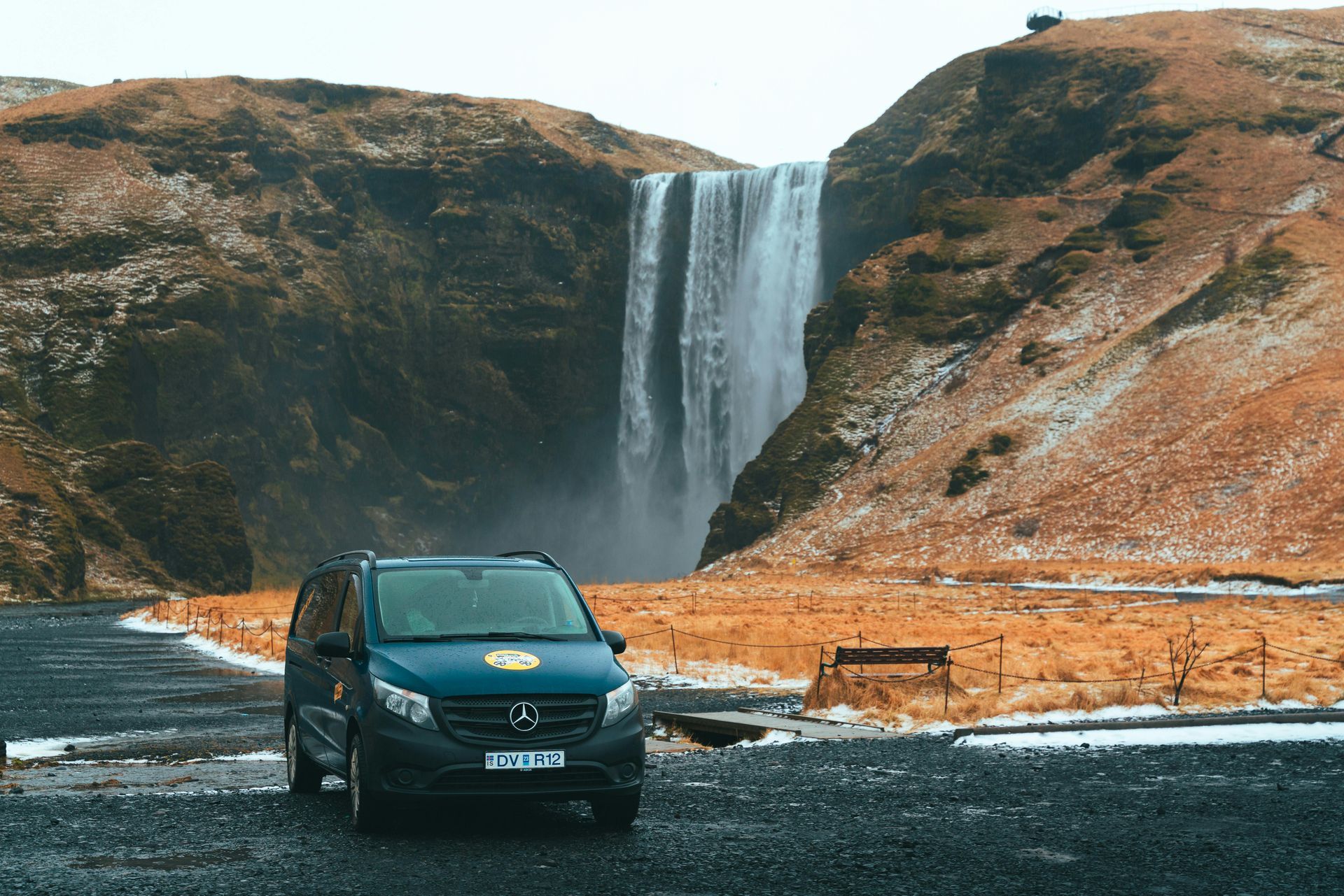 A blue van is parked in front of a waterfall in Iceland.