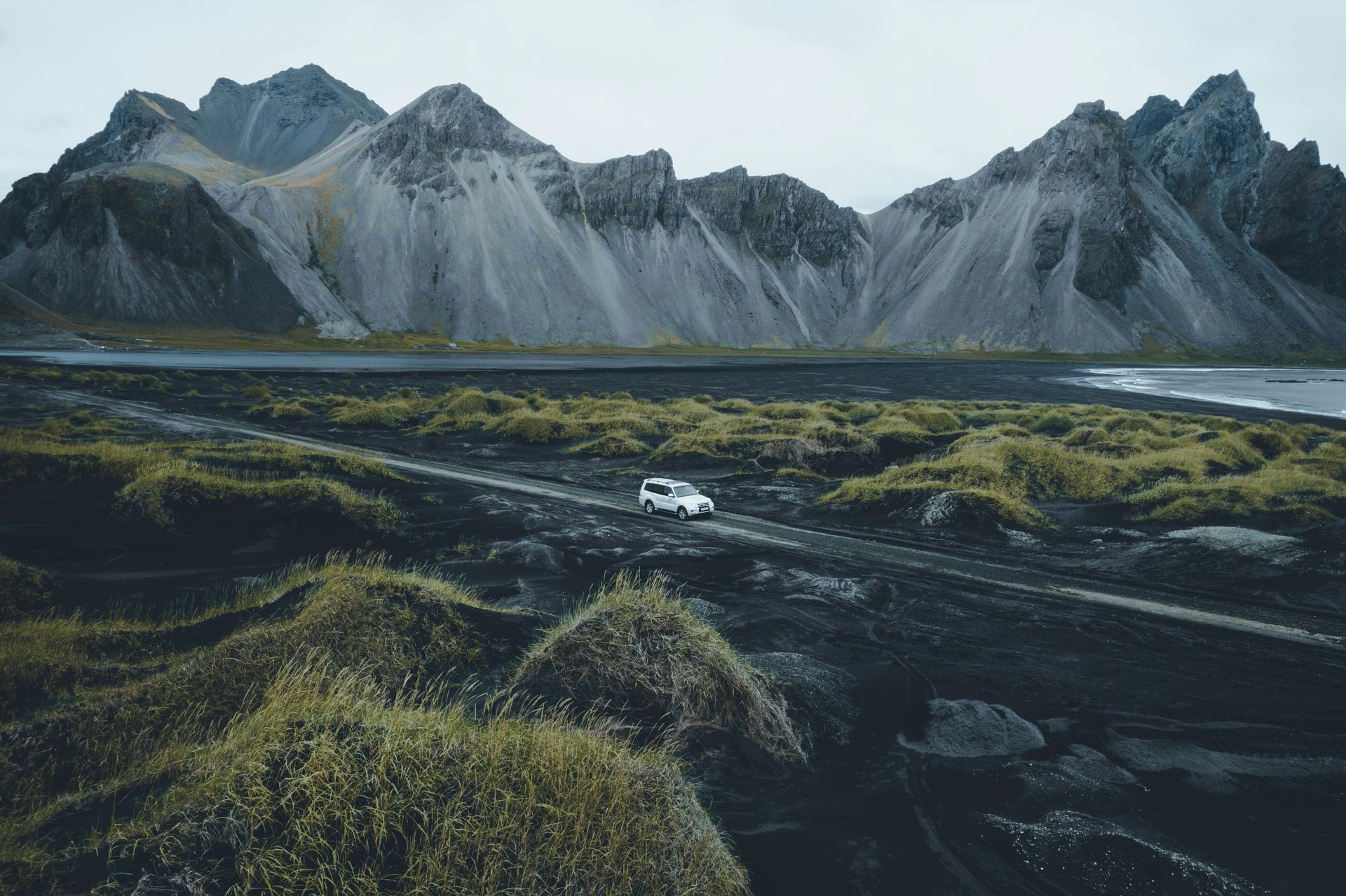 A van is driving down a dirt road in front of a mountain in Iceland.