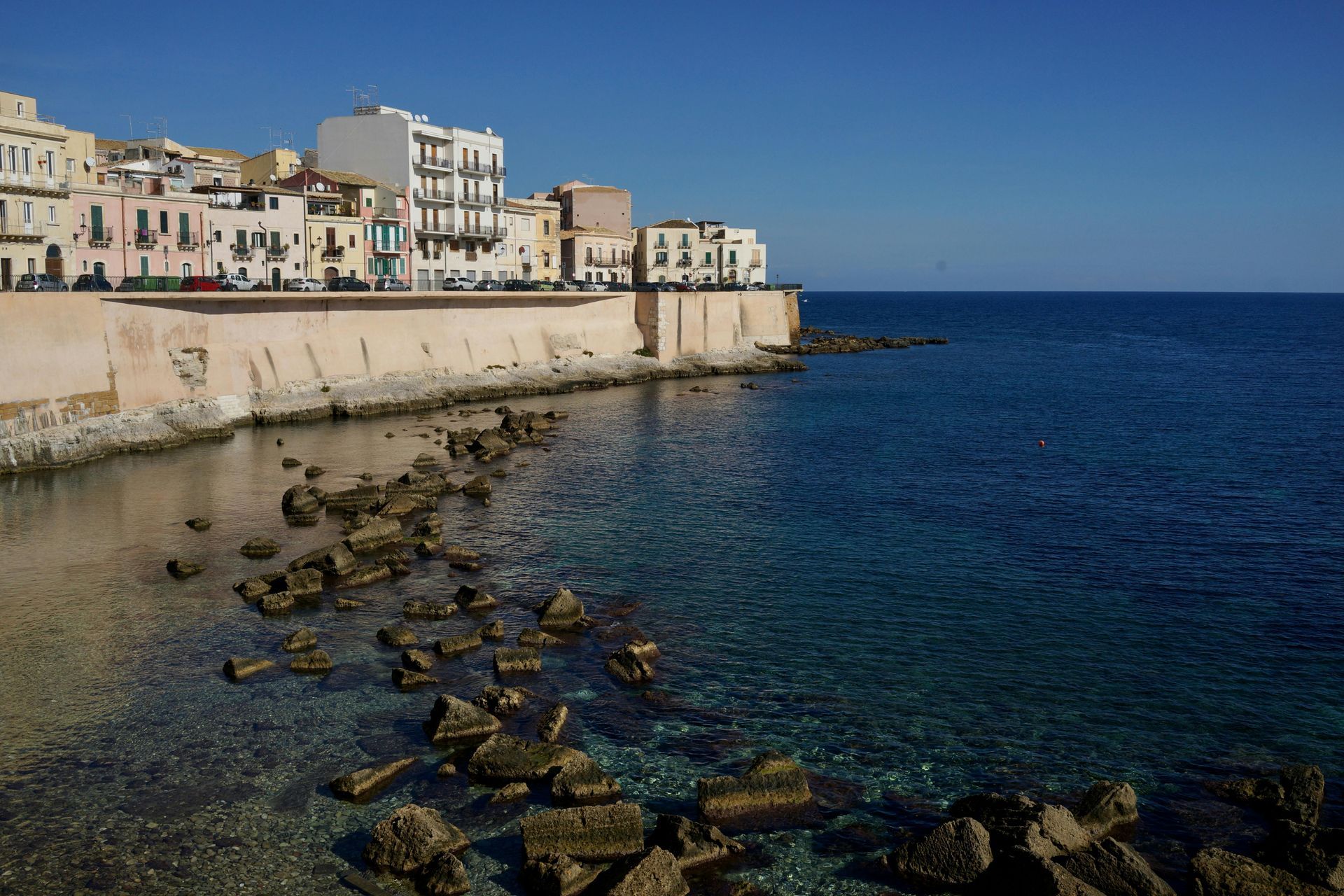 A cliff overlooking the ocean with buildings in the background in Sicily, Italy.