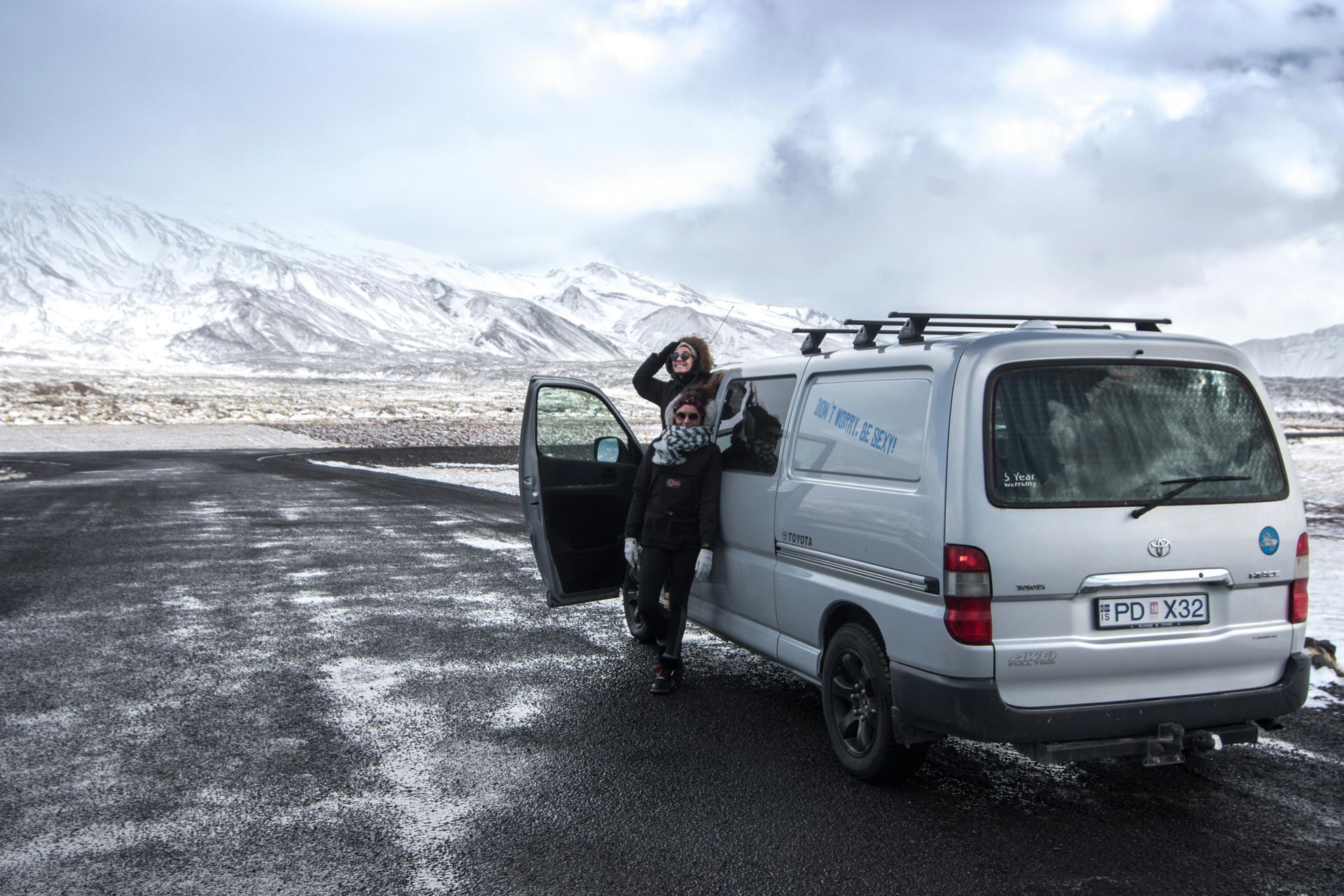 A woman is standing next to a white van on a snowy road in Iceland.