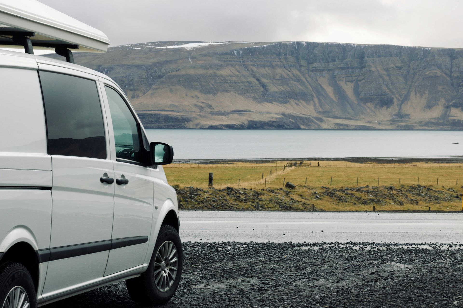 A white van is parked on the side of the road next to a lake in Iceland.