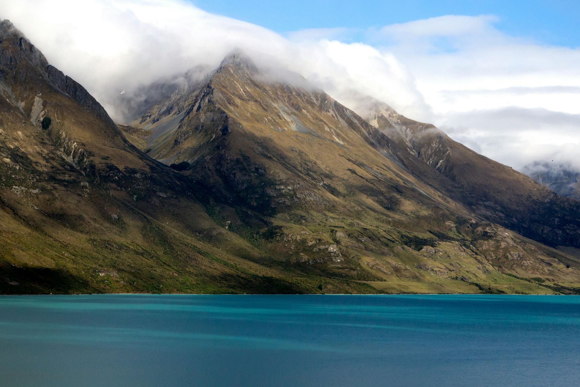 A lake surrounded by mountains and clouds with a mountain in the background in New Zealand.