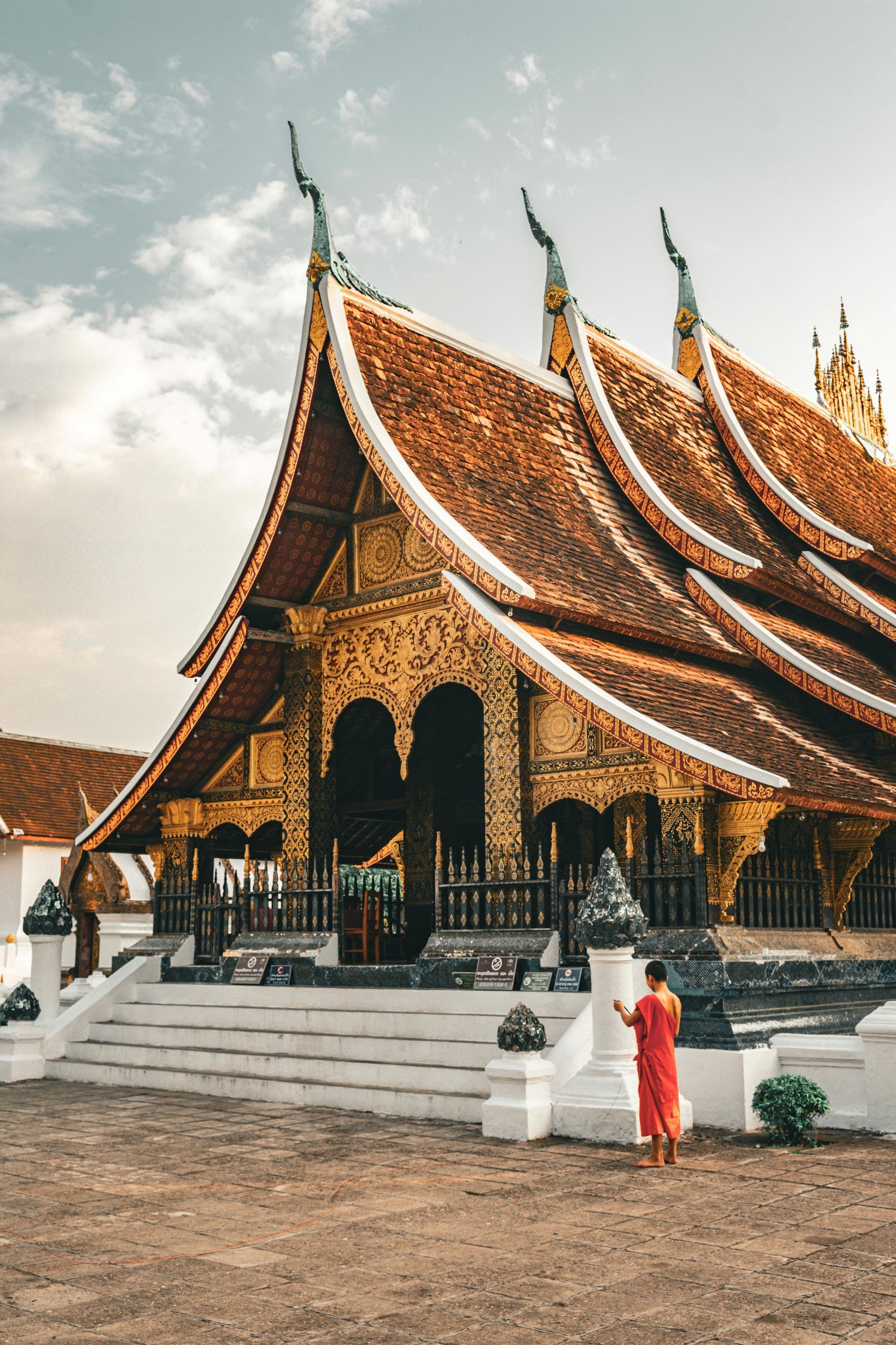 A man in a red robe is standing in front of Wat Xiengthong in Laos.