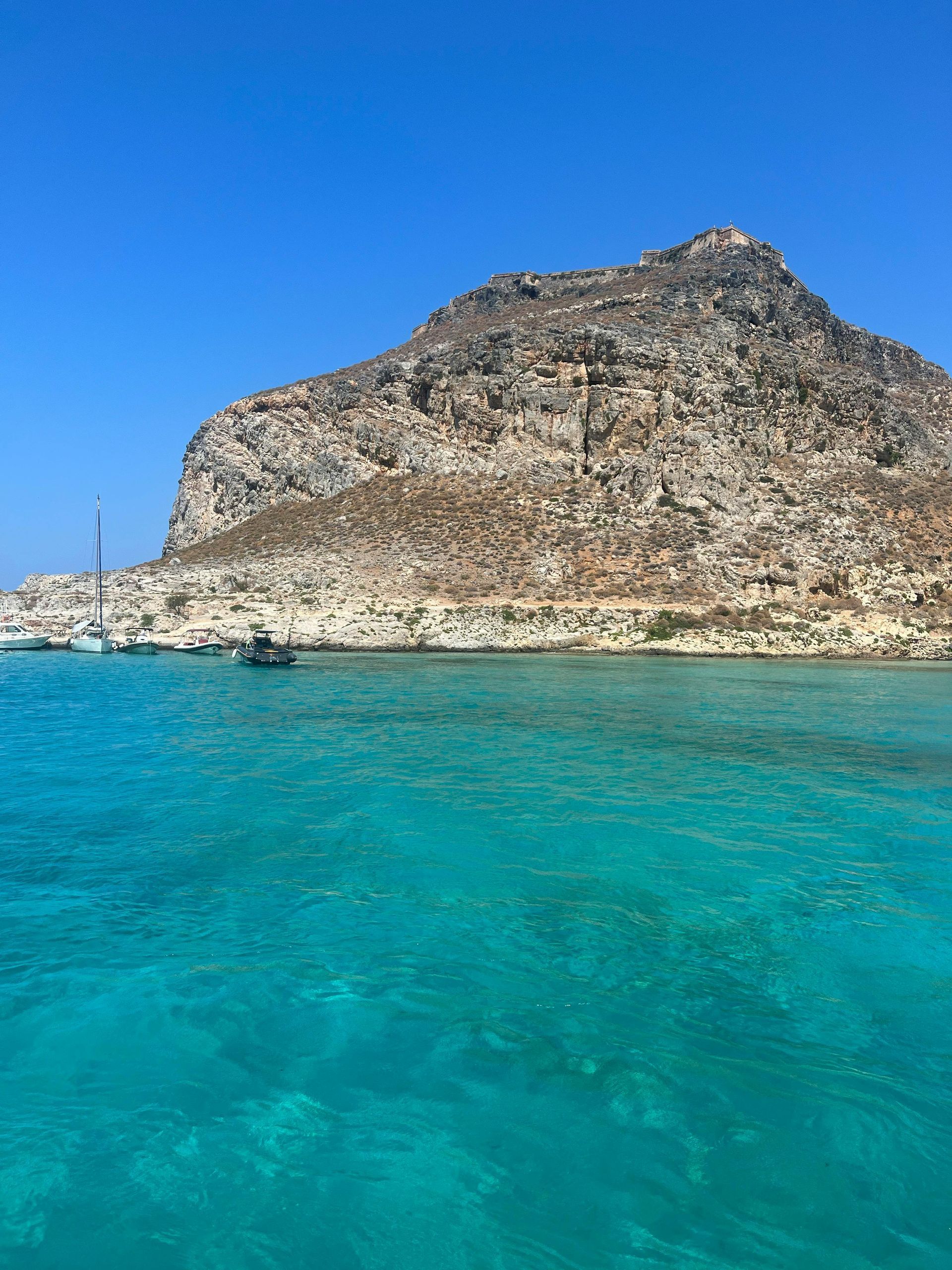 There is a mountain in the background and a boat in the water in Crete, Greece.