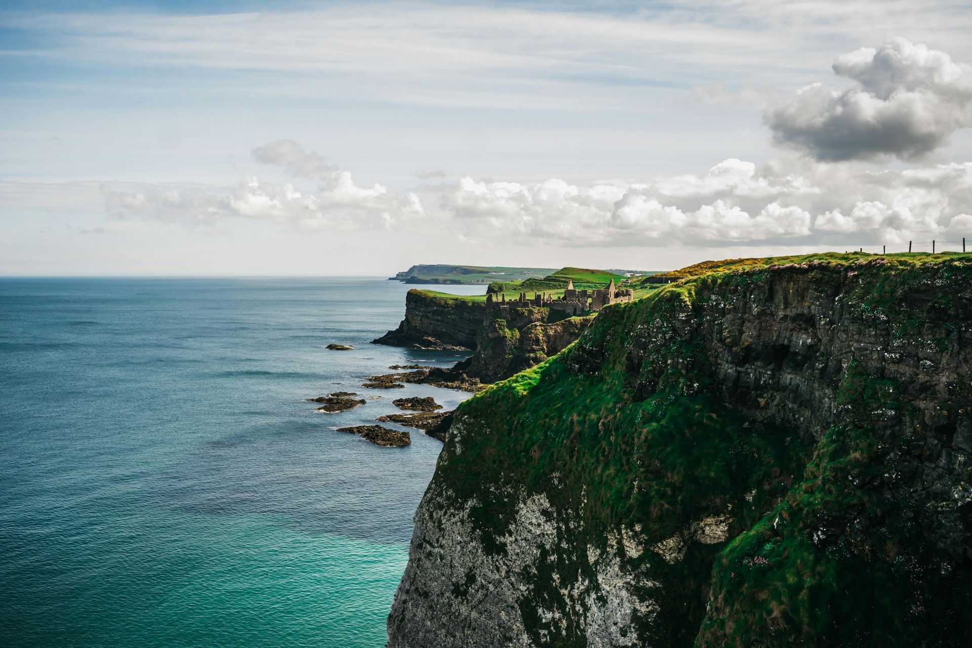 A view of the Cliffs of Moher overlooking the ocean with a castle in the distance in Ireland.