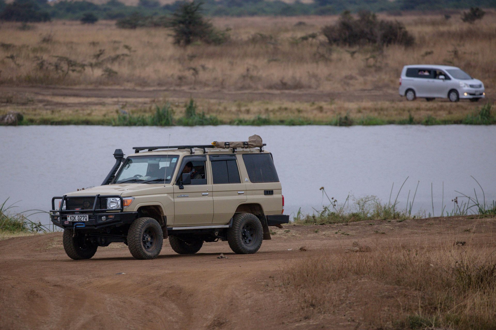 A jeep is driving down a dirt road next to a body of water in Kenya Africa.