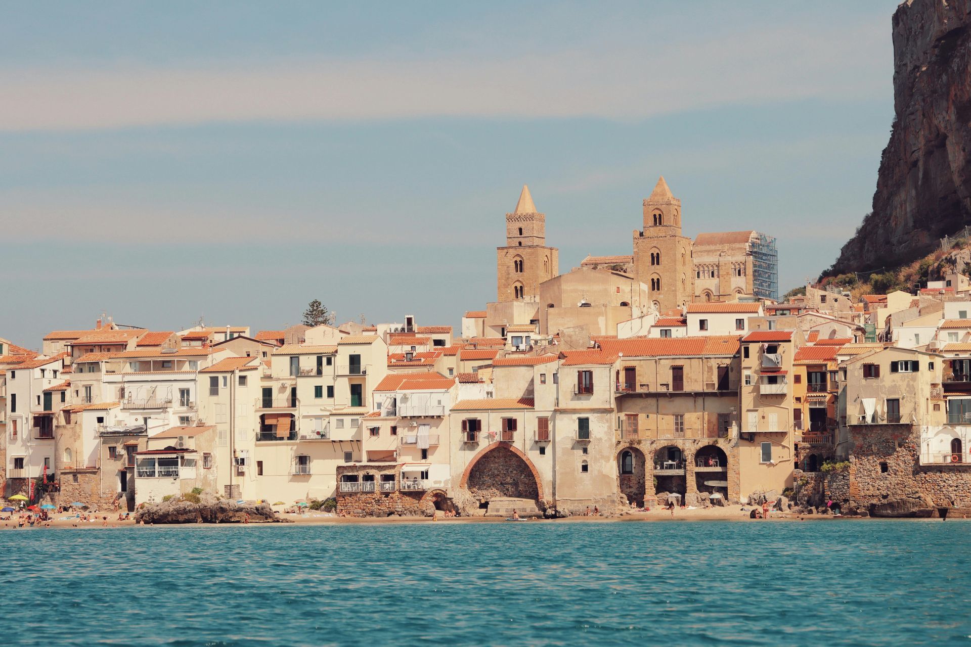 A small town is sitting on the shore of a large body of water in Sicily, Italy.