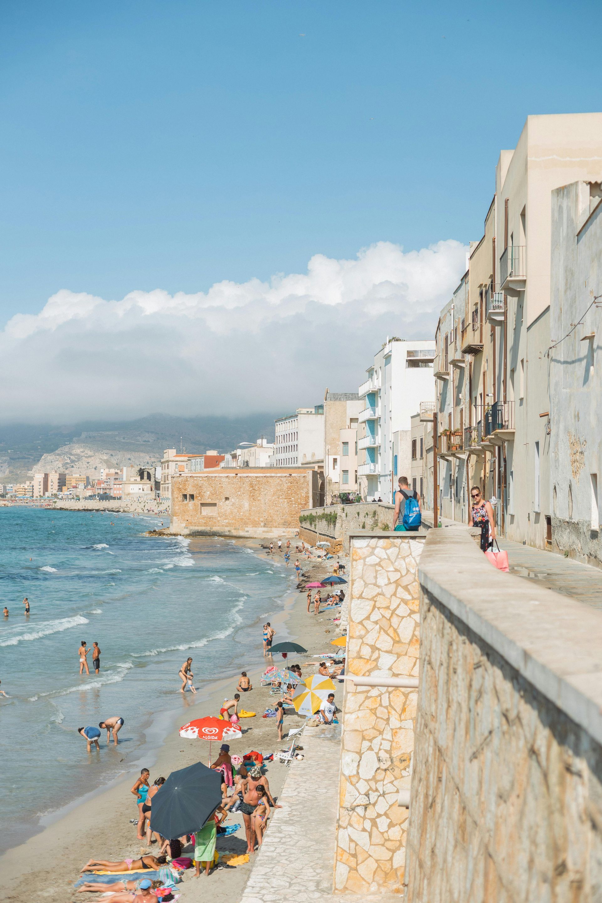 A beach filled with people and umbrellas on a sunny day in Sicily, Italy.