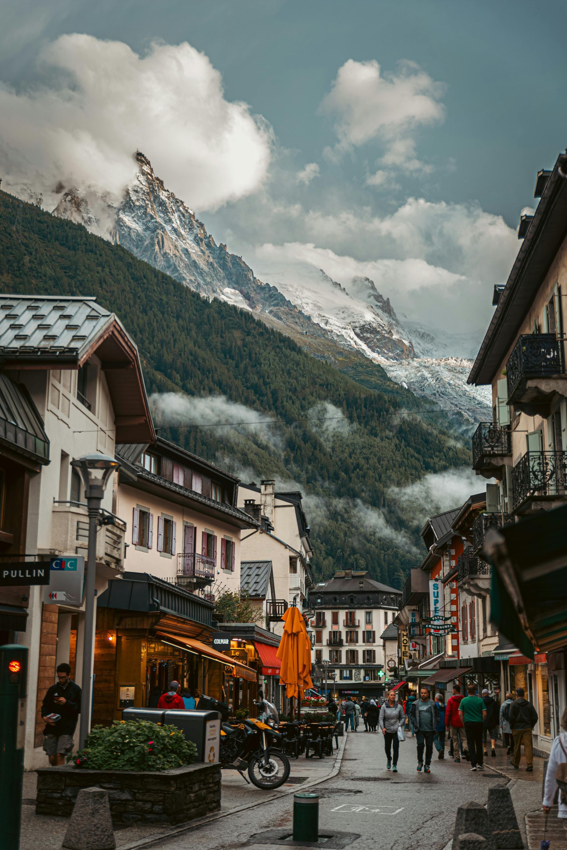 A city street with mountains in the background and people walking down it in Chamonix, France.