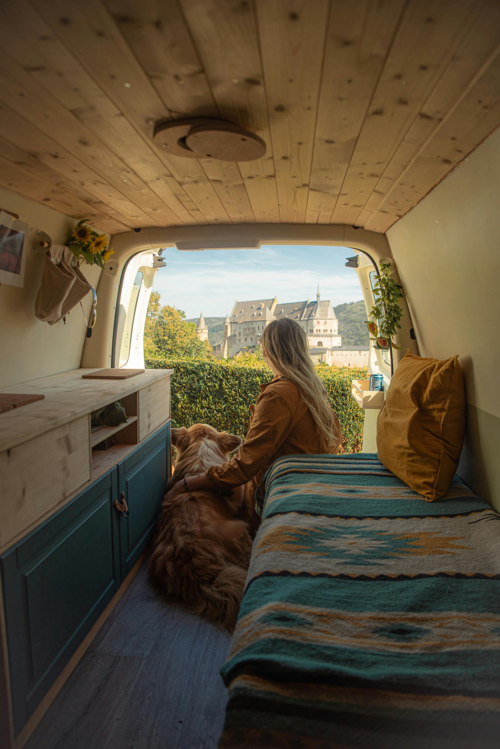 A woman is sitting on a bed in the back of a van with a dog in europe.