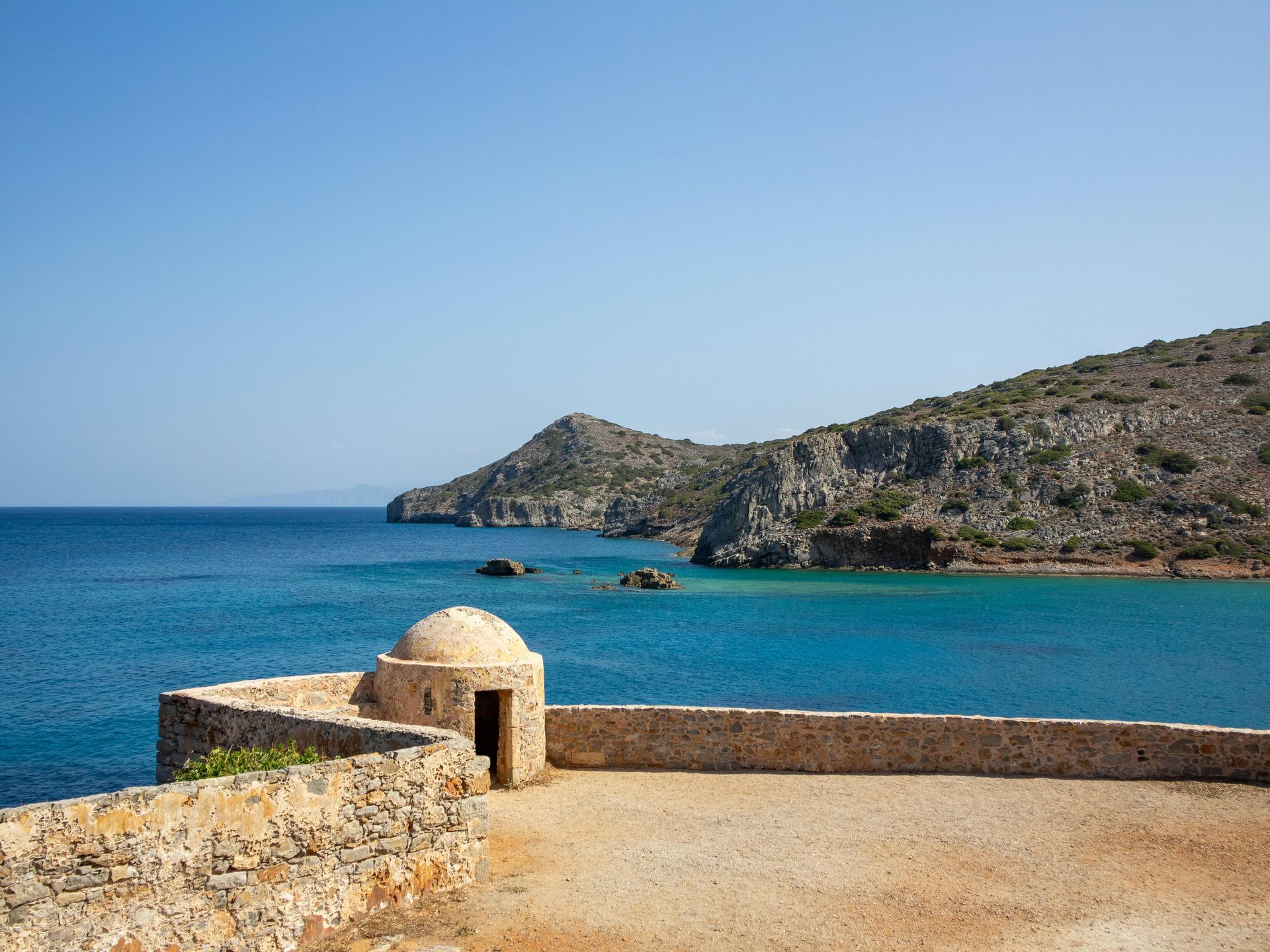 A stone wall surrounds a small island in the middle of the ocean in Crete, Greece.